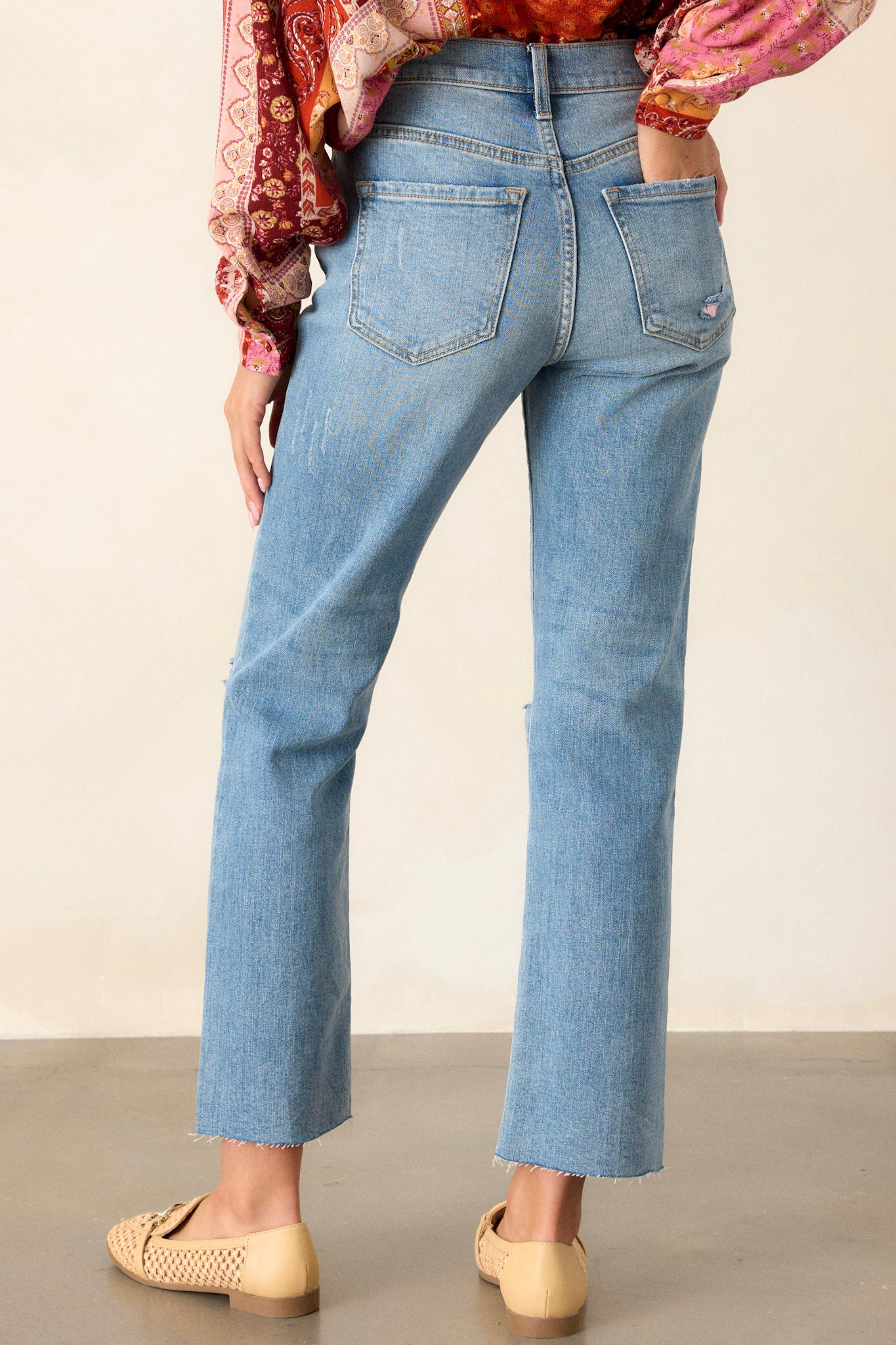 Back view of jeans highlighting the overall fit, functional back pockets, distressing, and raw hemline.