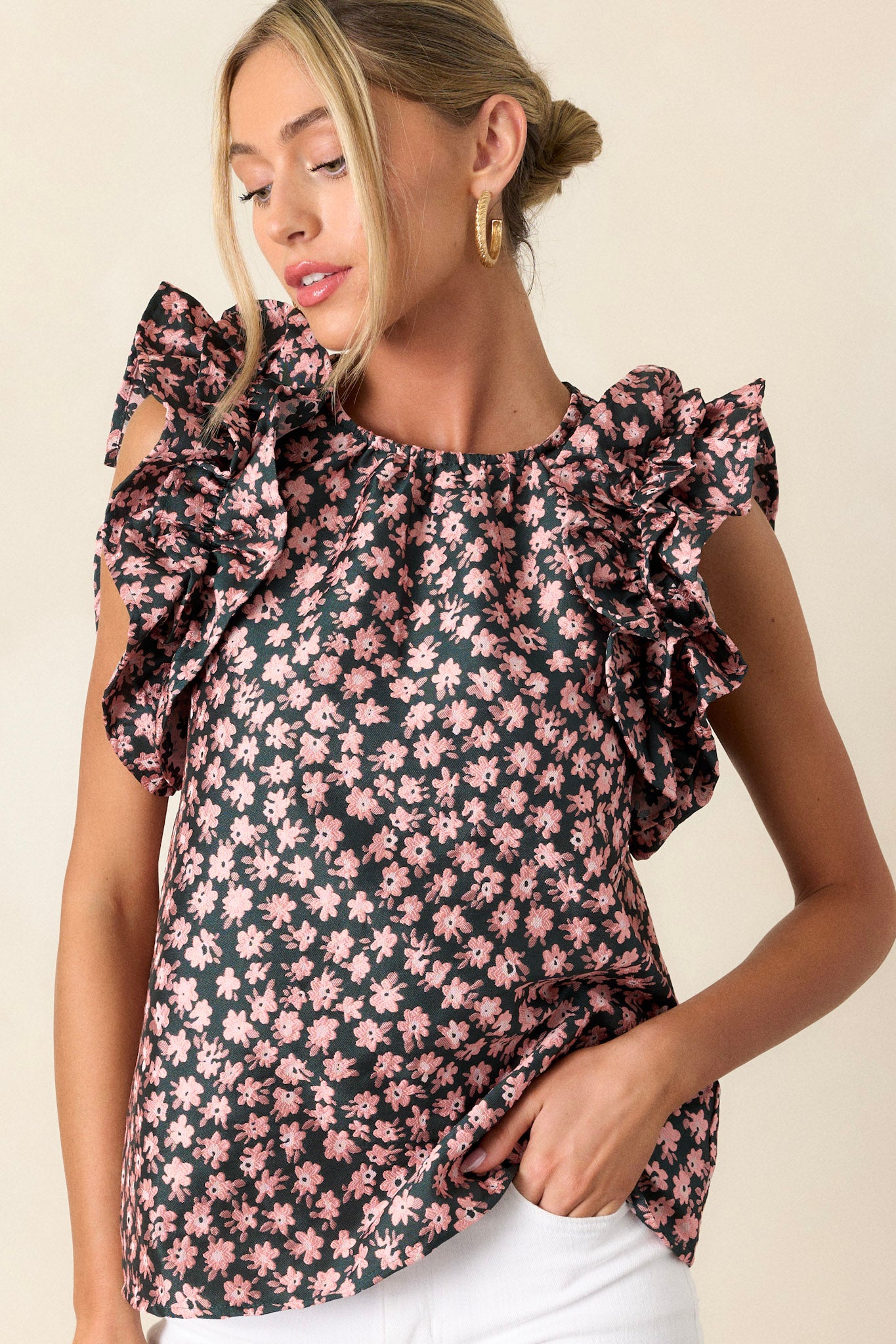 Front angled view of a hunter green floral top featuring a high rounded neckline, floral embroidery, and a ruffled sleeveless design