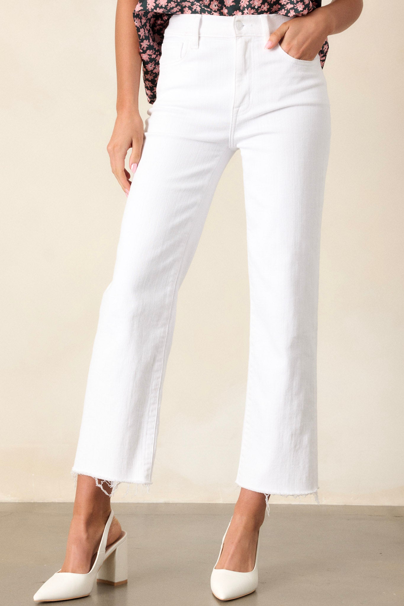 Front angled view of white jeans featuring a high waisted design, classic button and zipper closure, belt loops, functional front and back pockets, a cropped length, and a raw hemline