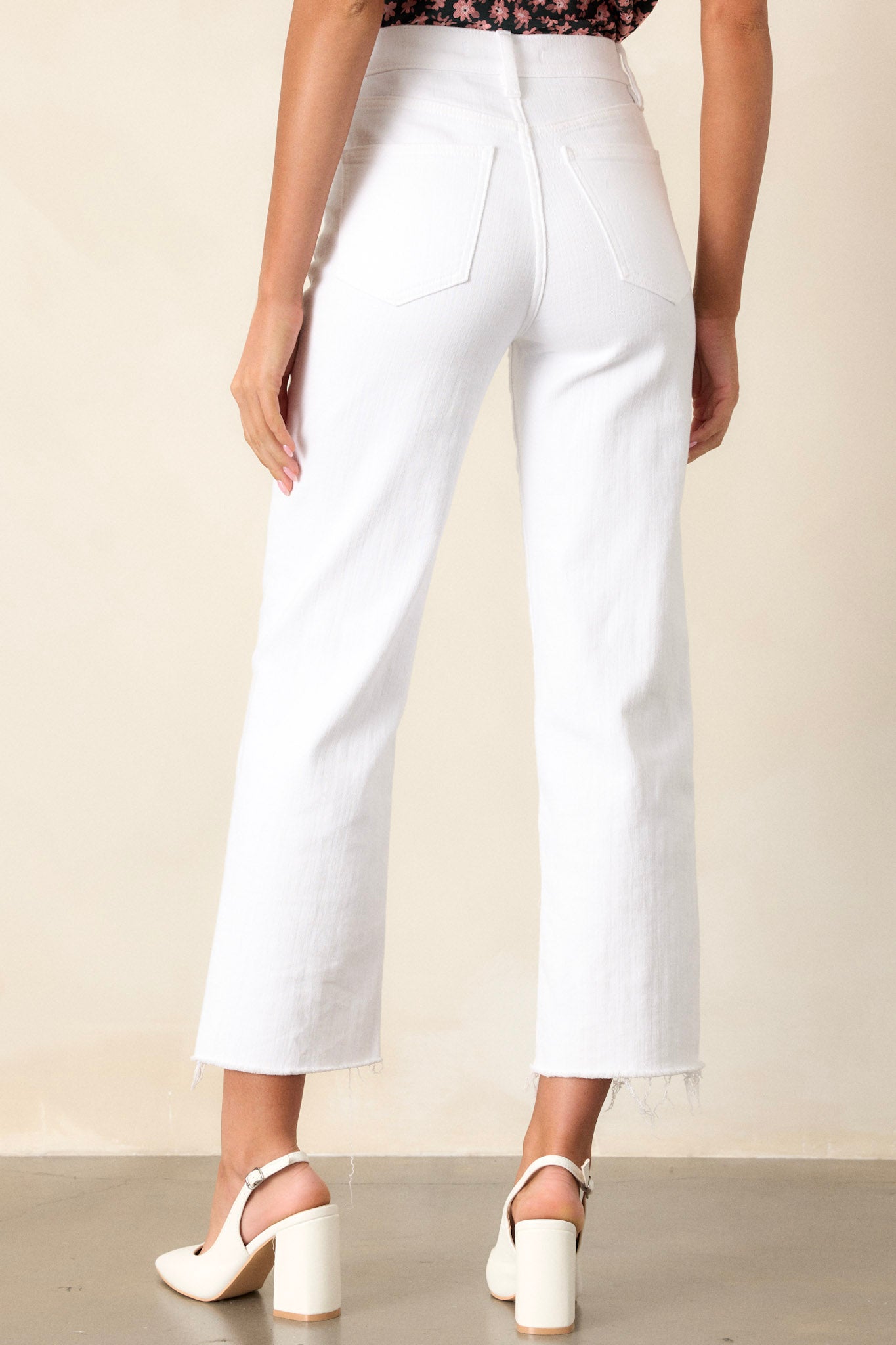 Back view of white jeans highlighting the high waisted design, belt loops, functional back pockets, and the cropped length with a raw hemline.