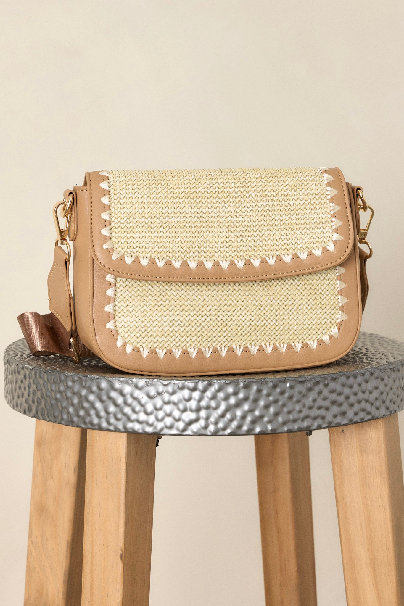 This tan woven handbag features a magnetic flap closure, two inside pockets, gold hardware, and an optional crossbody strap.