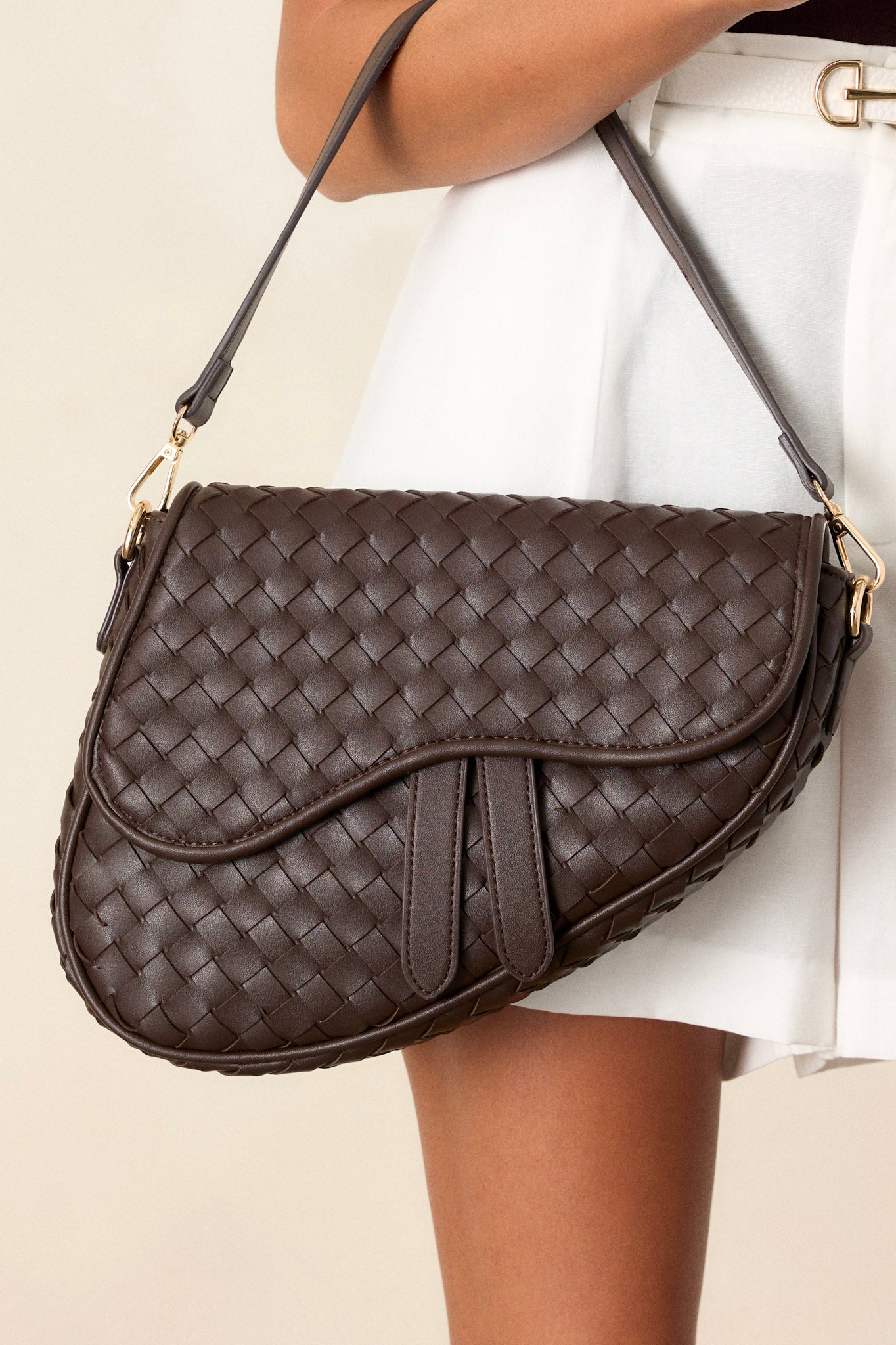 Front view of this brown handbag that features gold hardware, faux leather, a woven design, a magnetic snap closure, a zipper pocket, and an additional strap.