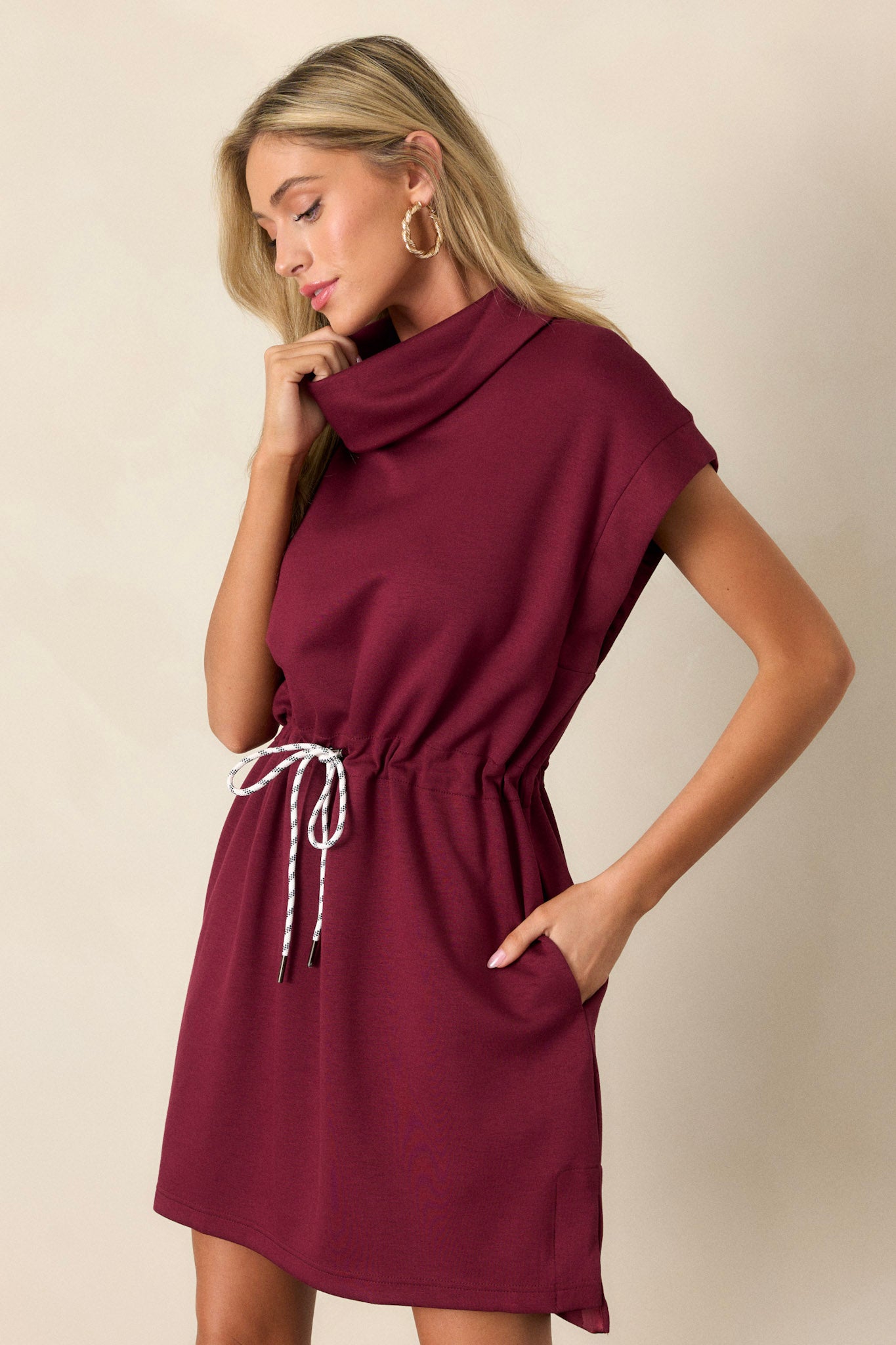 Chic burgundy mini dress with short cap sleeves, a drawstring waist, cowl turtleneck, and practical pockets for everyday wear.