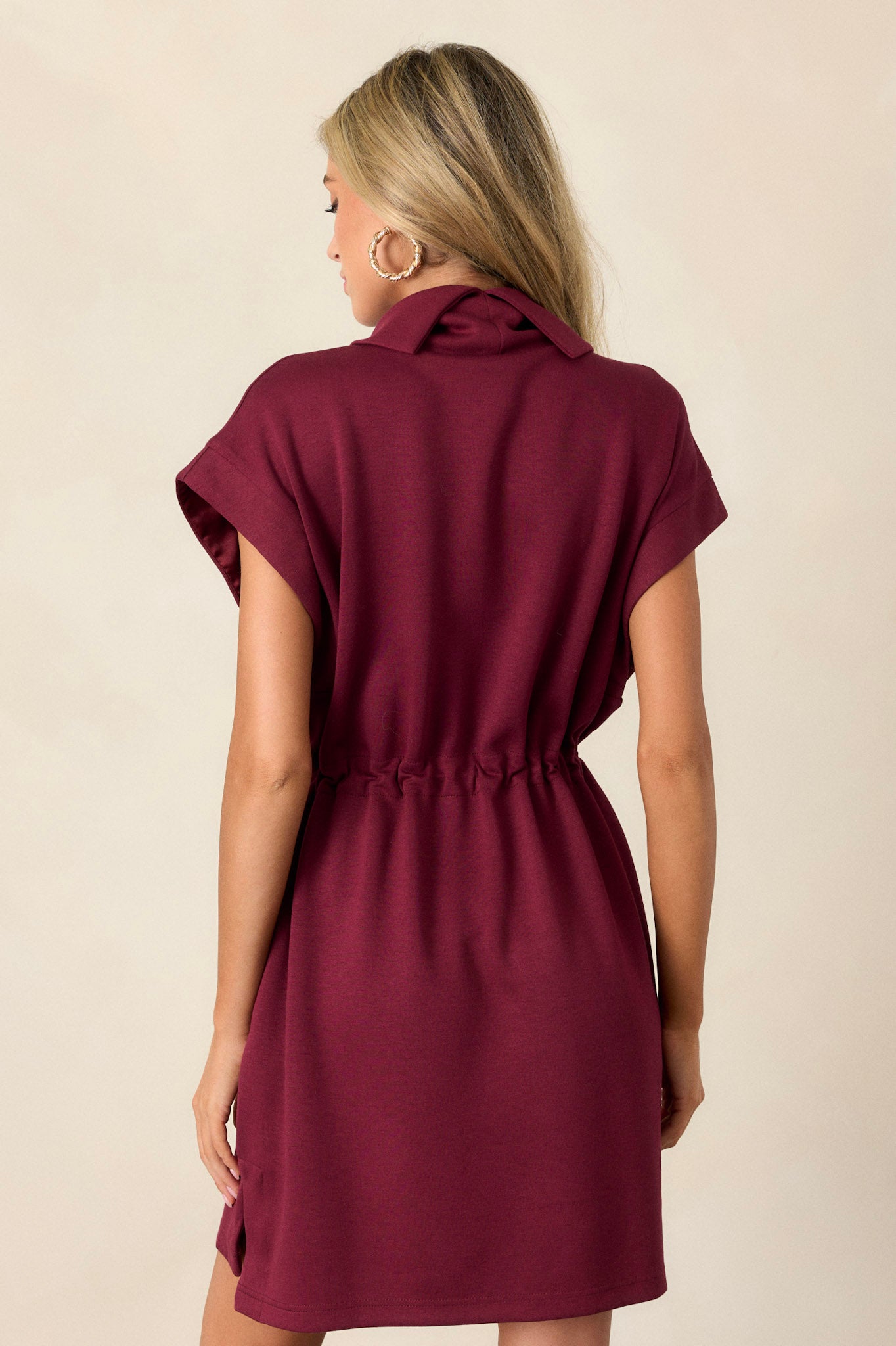 Back view of this burgundy dress with short sleeves, drawstring waist, cowl turtleneck, and pockets, perfect for any occasion.