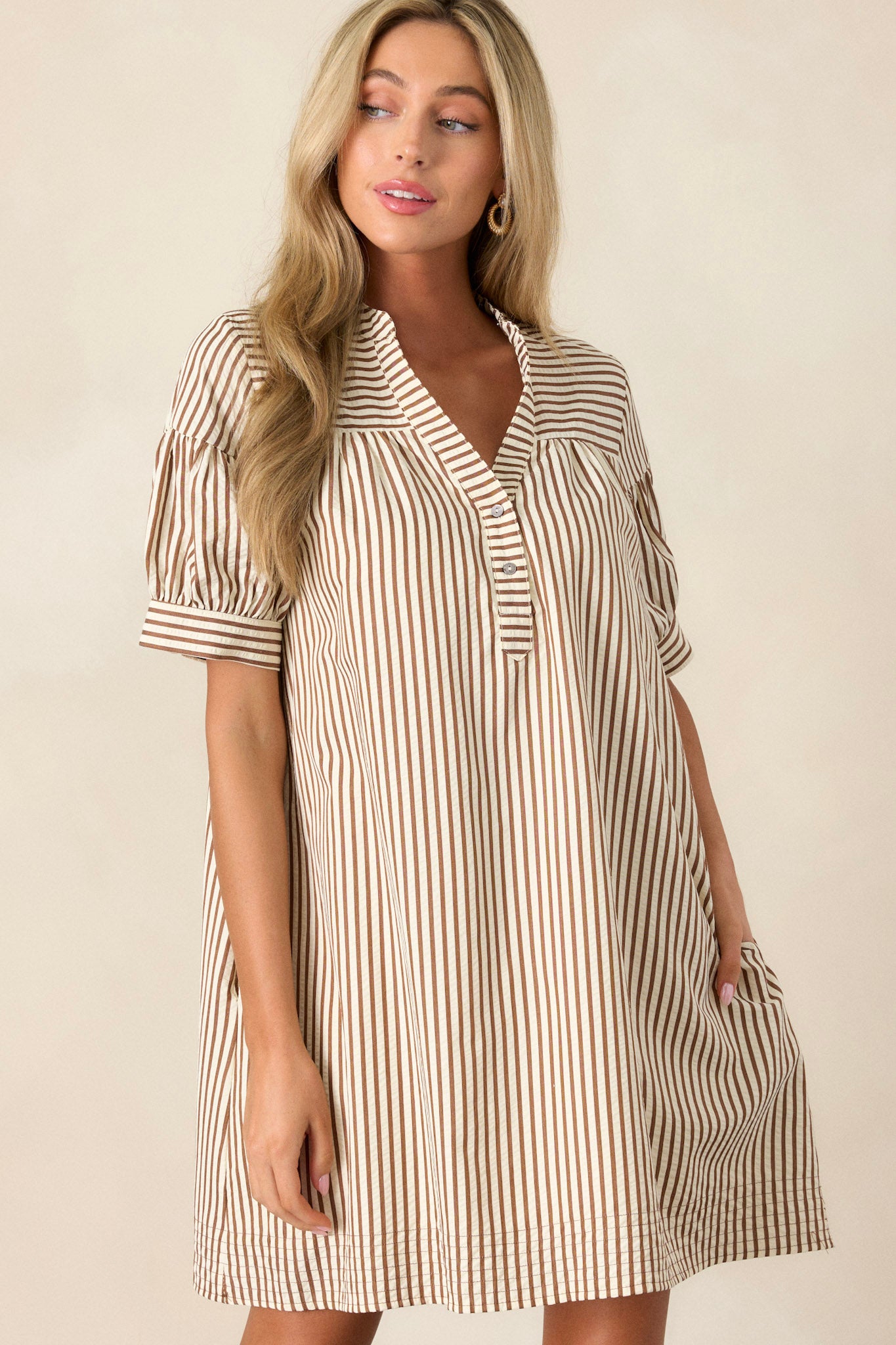 Front angled view of the brown stripe dress featuring a v-neckline, button-up bust, relaxed fit, vertical brown and white stripe design, and short sleeves