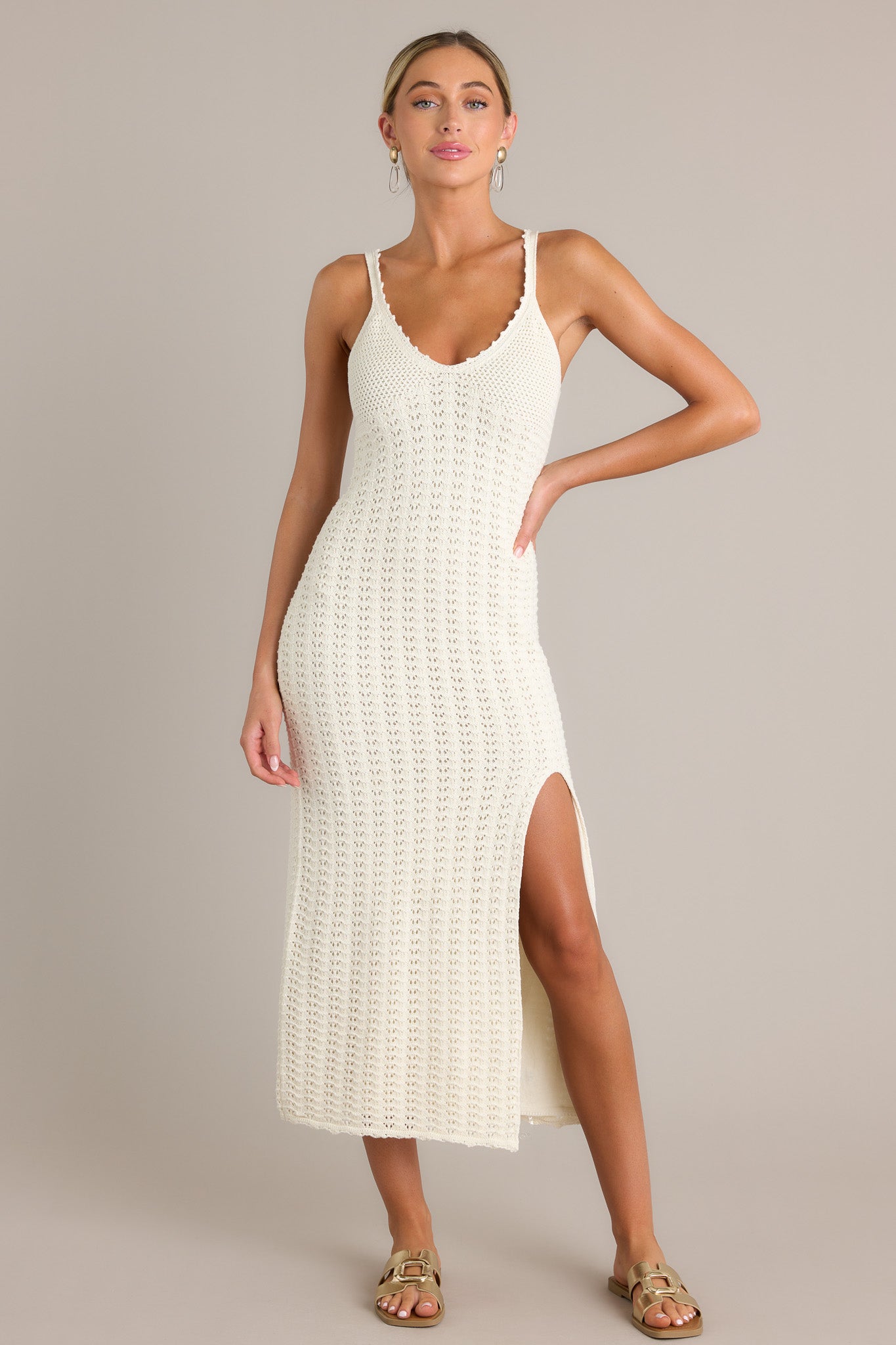 Front view of this sandstone midi dress featuring a v-neckline, thin straps, a unique crochet design, and a side slit.