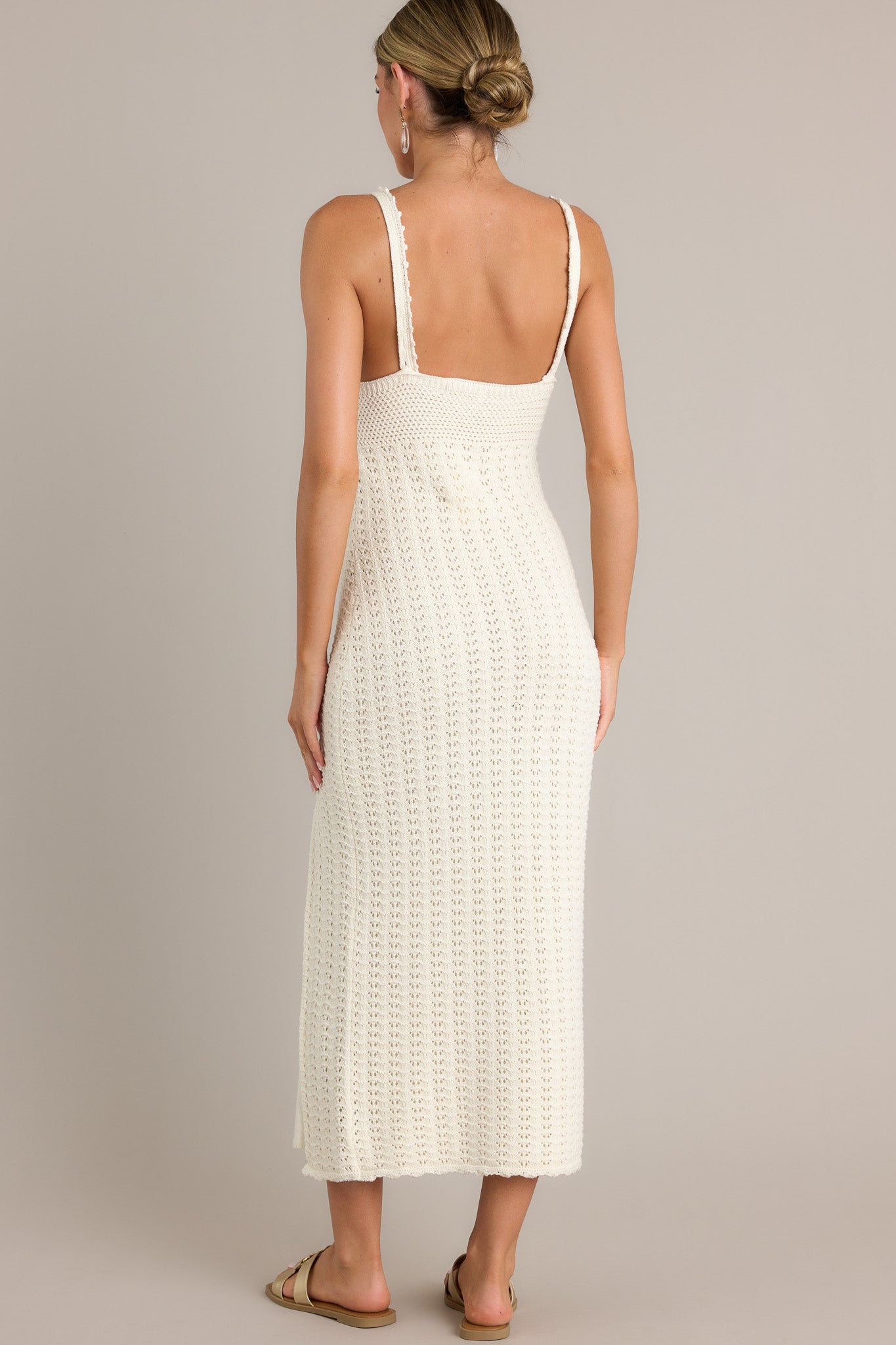 Back view of this sandstone midi dress featuring a v-neckline, thin straps, a unique crochet design, and a side slit.