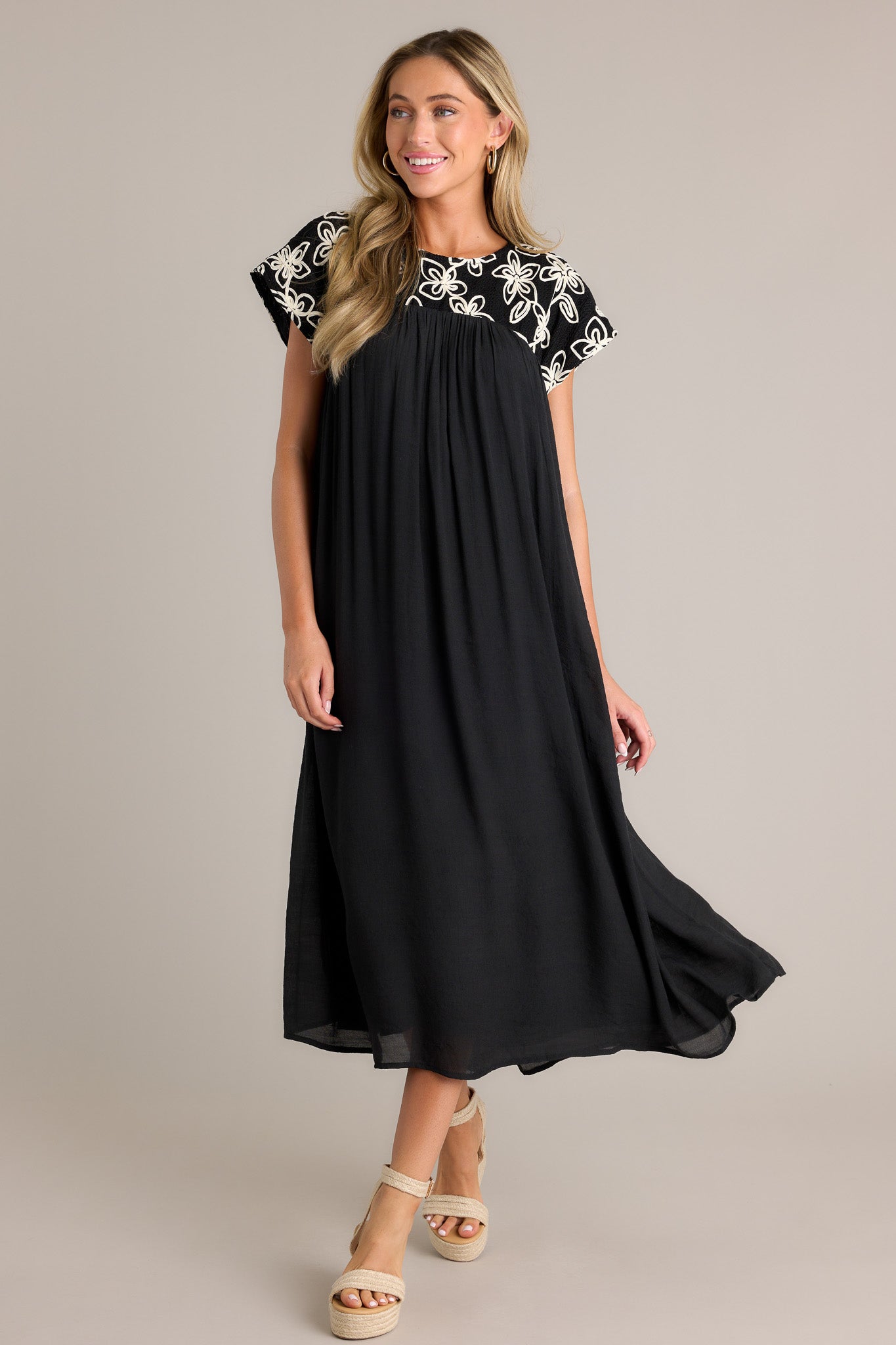 Front view of the black midi dress showcasing a high rounded neckline, embroidered floral pattern, and short sleeves.