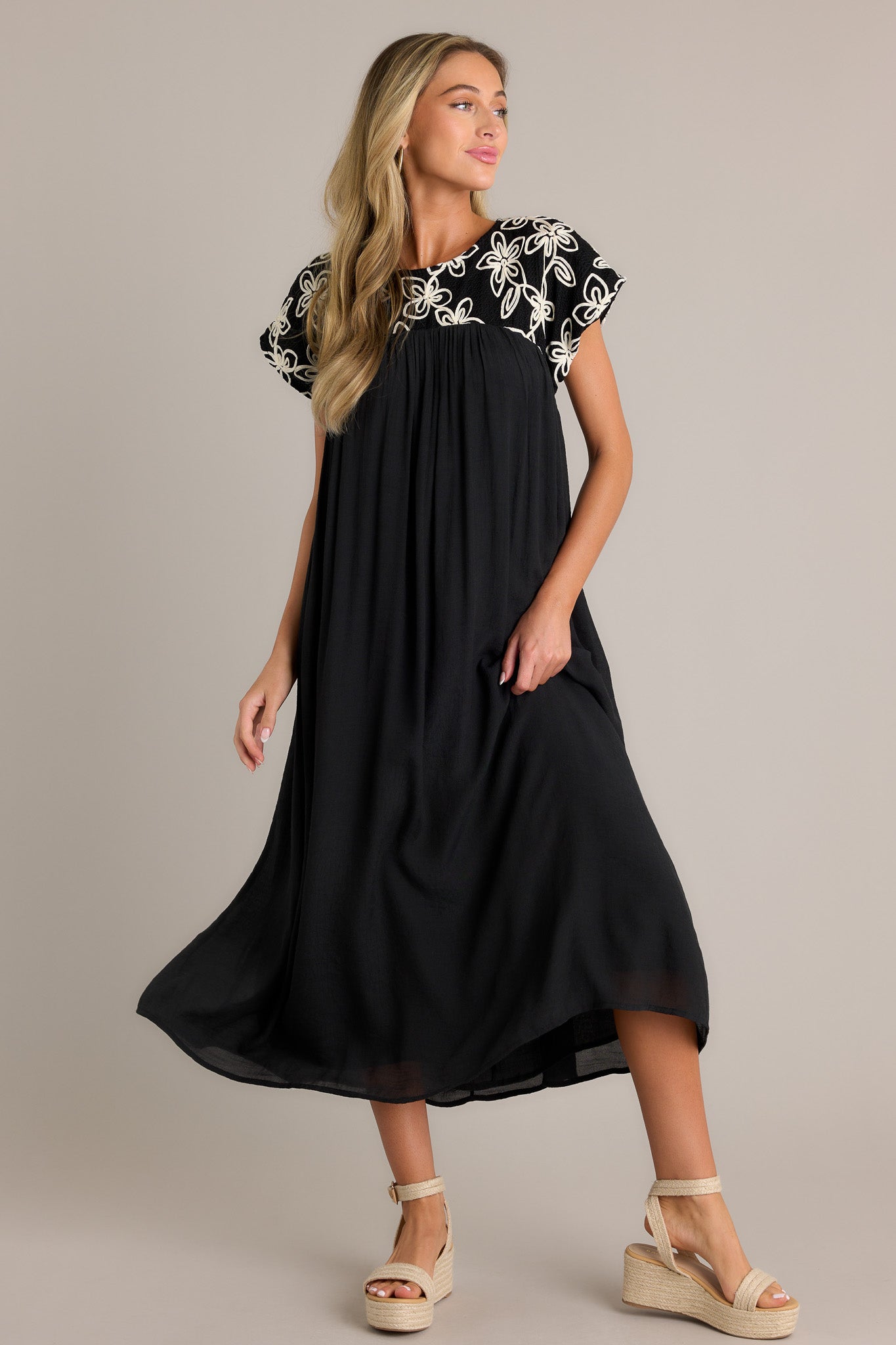 Black midi dress with a high rounded neckline and embroidered floral pattern, featuring a flowing silhouette and short sleeves.