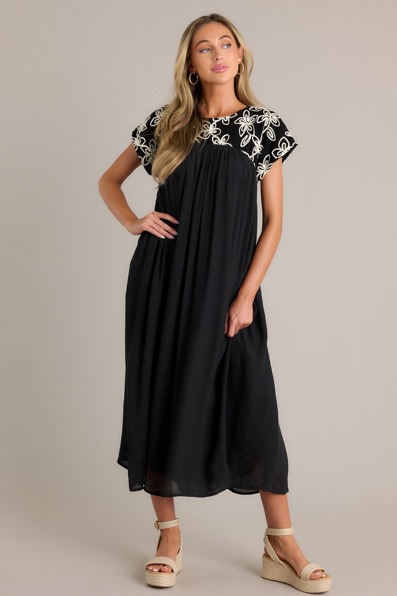 Flowing black midi dress featuring a high rounded neckline, short sleeves, and an intricate embroidered floral pattern