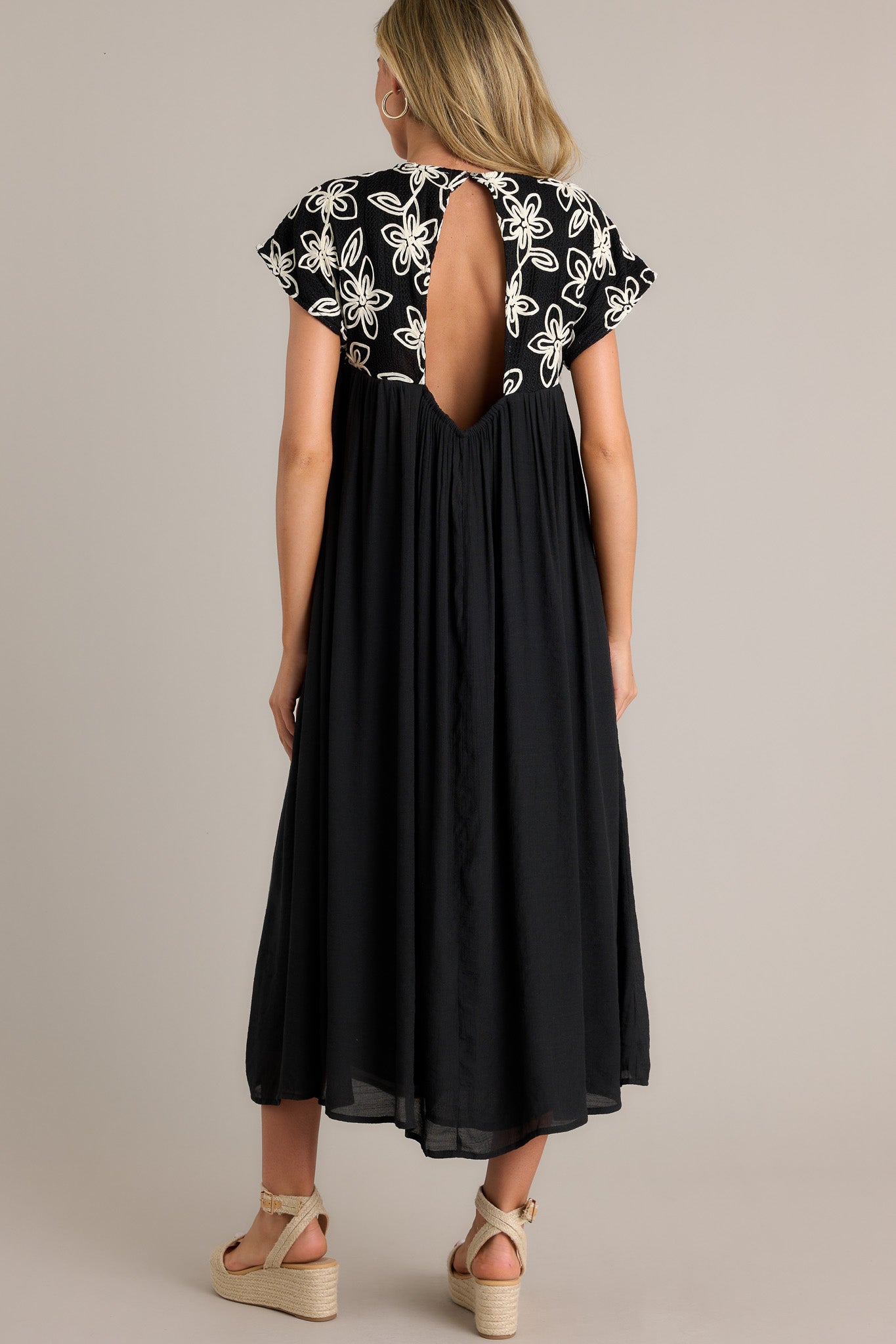 Back view of the black midi dress highlighting the high rounded neckline, embroidered floral pattern, and flowing silhouette.