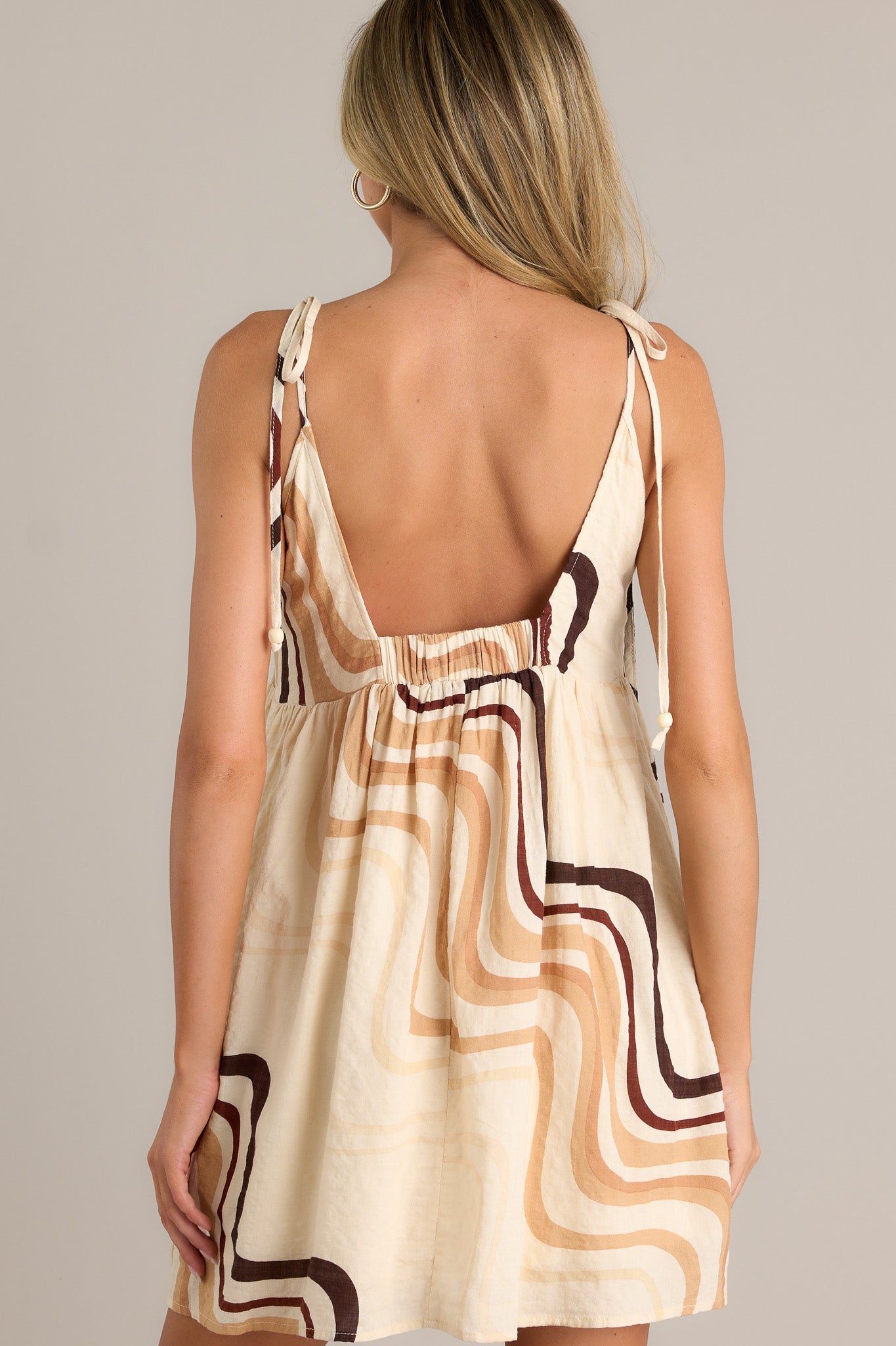 Back view of a beige mini dress highlighting the elastic back insert, thin self-tie straps, and overall fit.