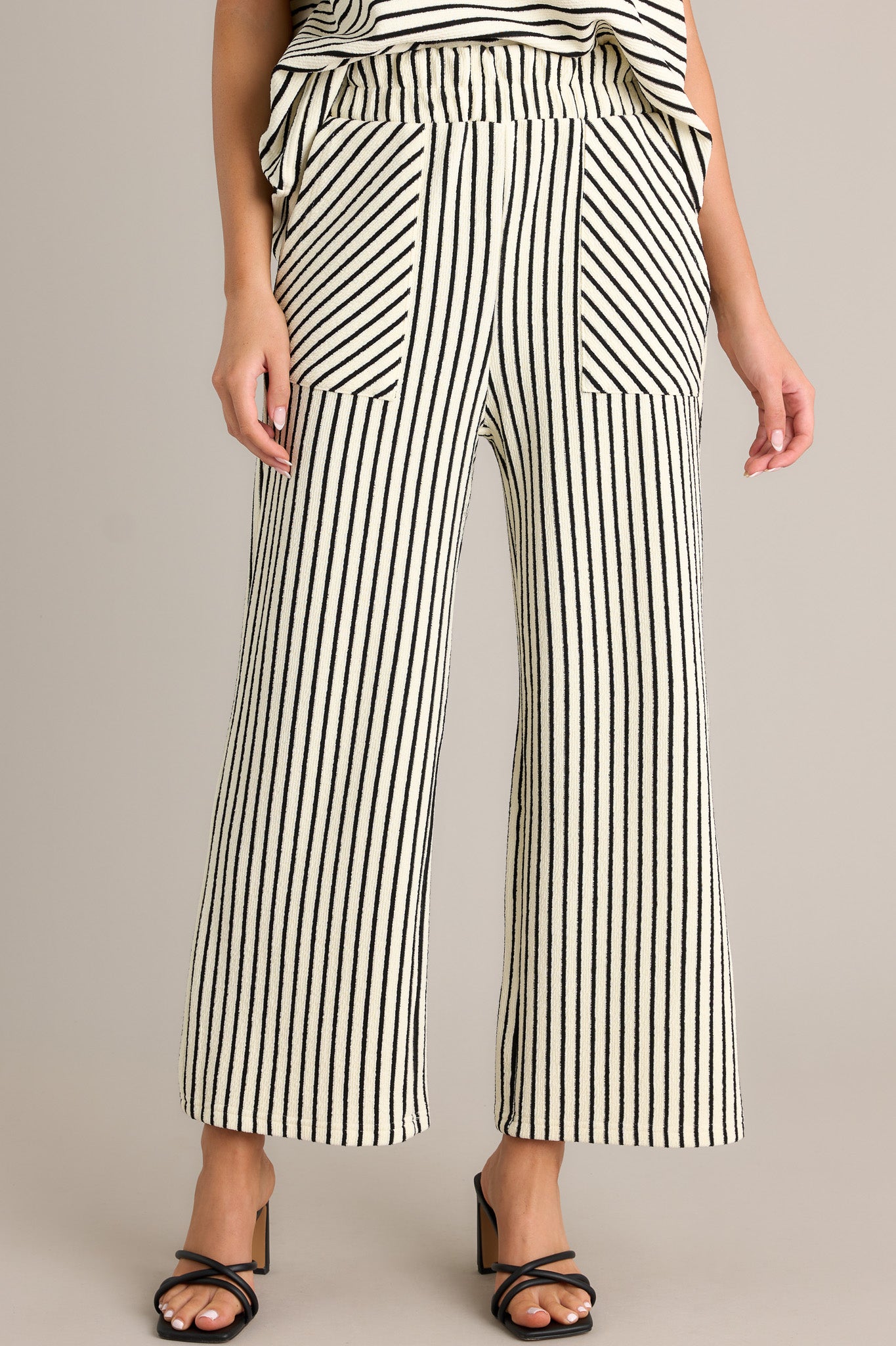 Front view of black stripe pants featuring a high waisted design, an elastic waistband, a self-tie drawstring, functional hip pockets, and a wide leg.