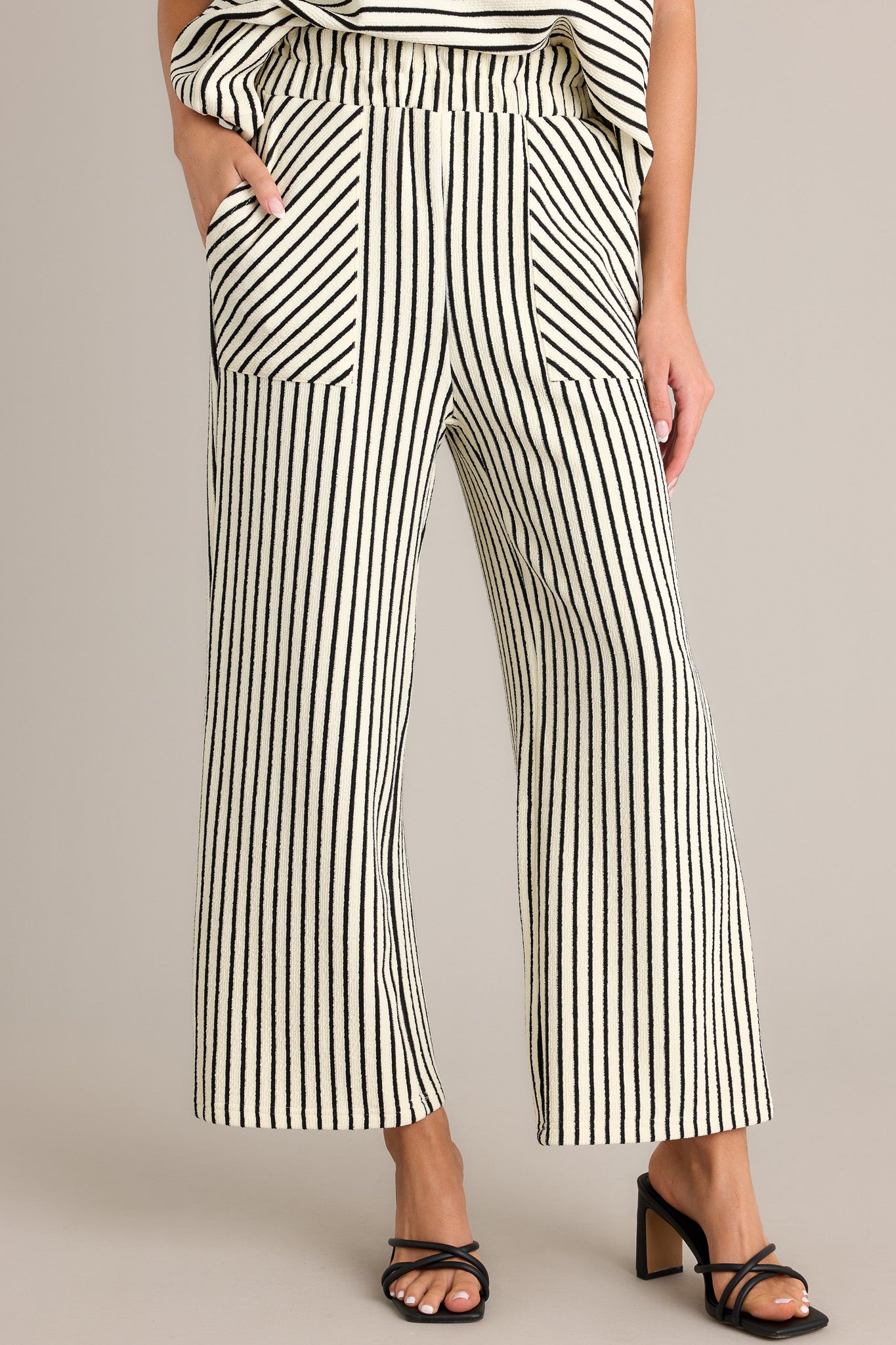 Front angled view of black stripe pants featuring a high waisted design, an elastic waistband, a self-tie drawstring, functional hip pockets, and a wide leg