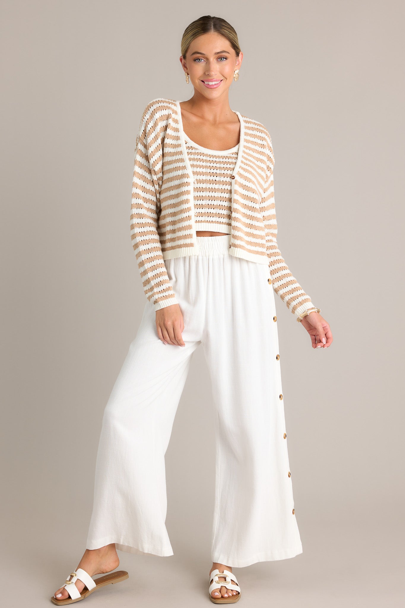 These ivory pants feature a high waisted design, an elastic waistband, functional buttons all down the sides, a lightweight material, and a wide leg.