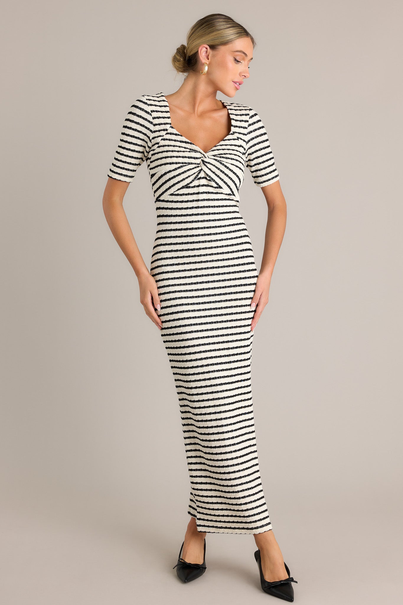 Movement view of this black stripe maxi dress featuring a v-neckline, a twisted bust detail, a bodycon fit, a textured fabric, a side slit, and short sleeves.