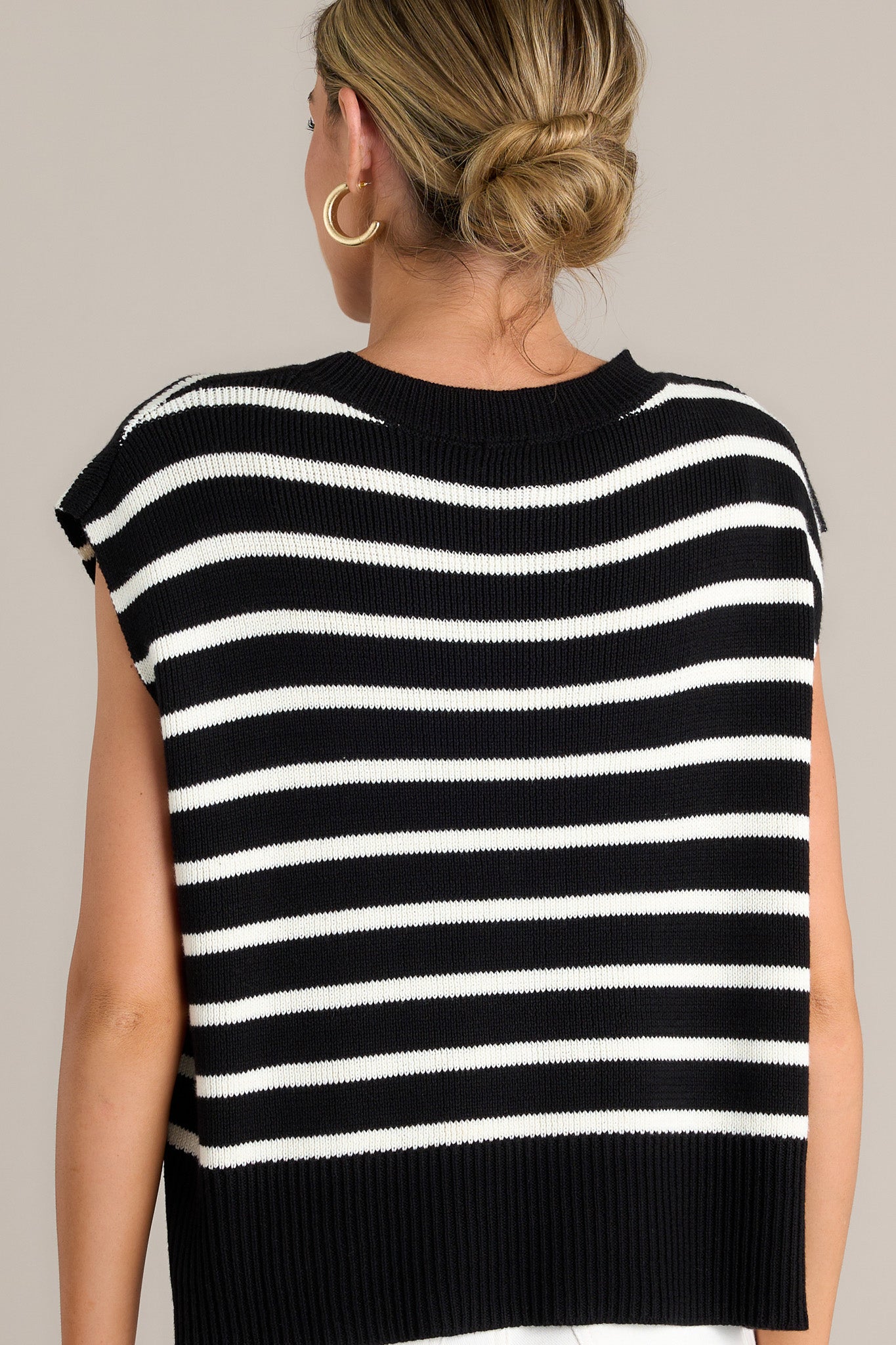 Back view of this black sweater top featuring a ribbed crew neckline, horizontal white stripes, a split ribbed hemline, and short sleeves.