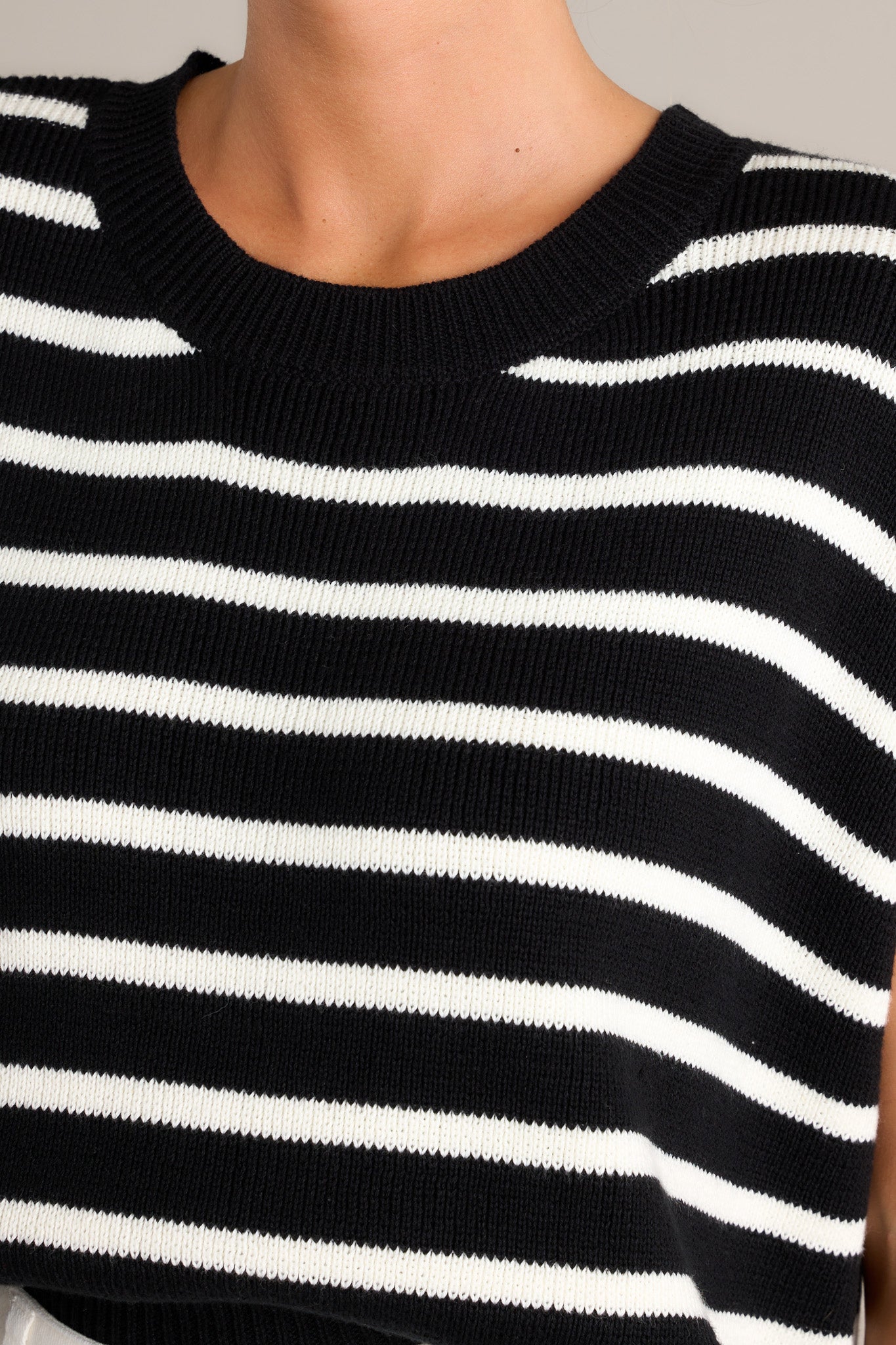 Detail shot of the knit fabric and crew neck on this lack sweater with white horizontal stripes.