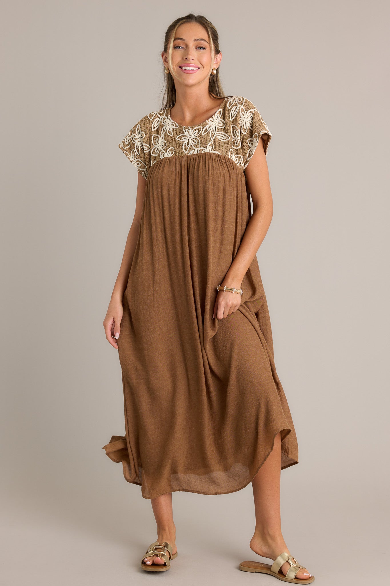 Tan midi dress with a high rounded neckline and embroidered floral pattern, featuring a flowing silhouette and short sleeves.