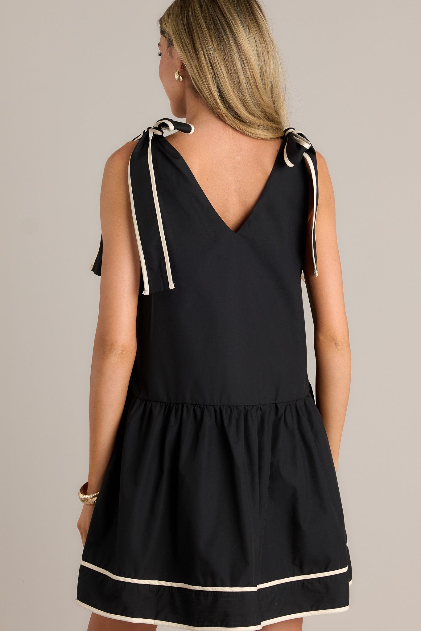 Back view of the black mini dress highlighting the thick self-tie shoulder straps and the high contrast trim along the edges.