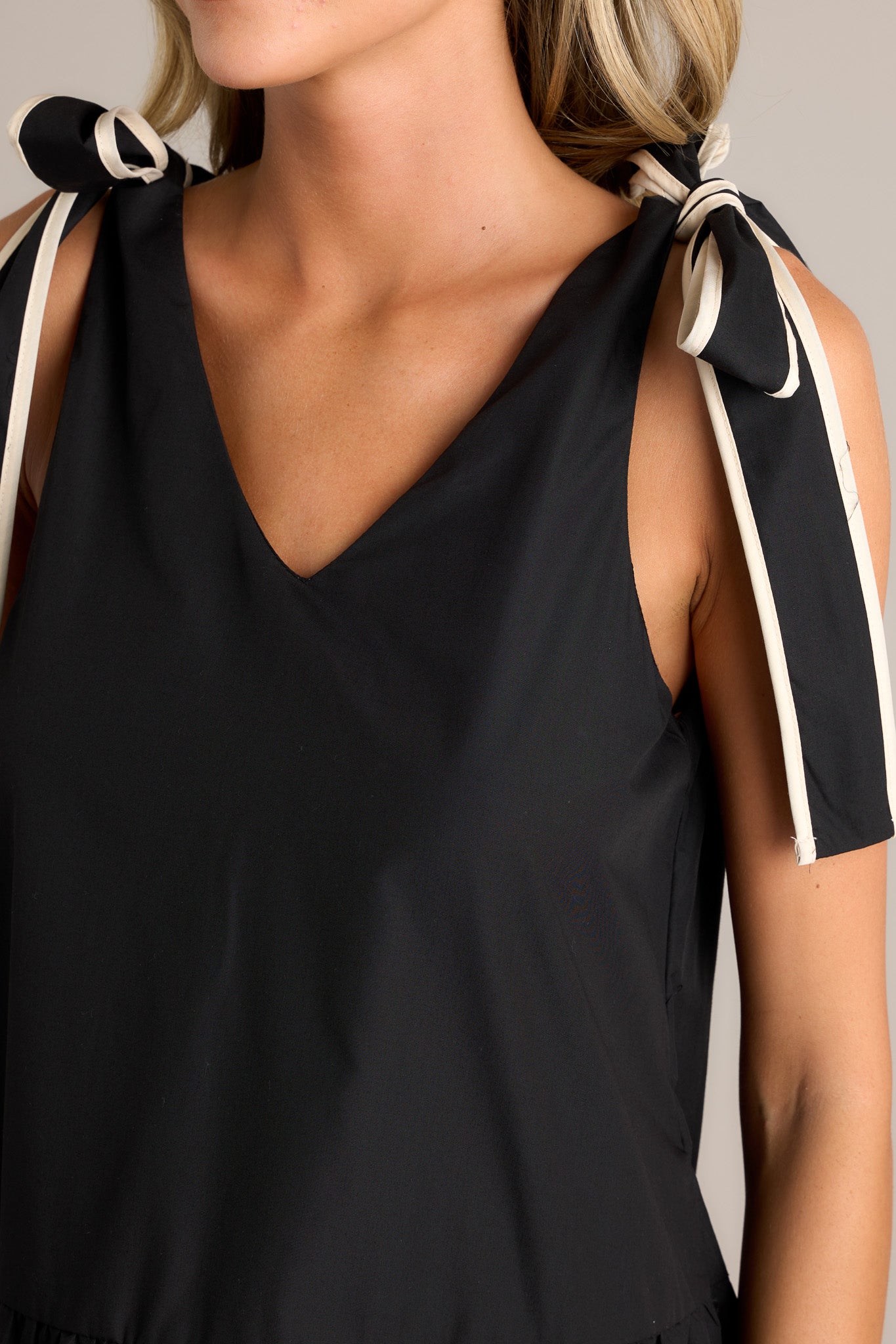 Close-up detail of the black mini dress showing the v-neckline and the high contrast trim.