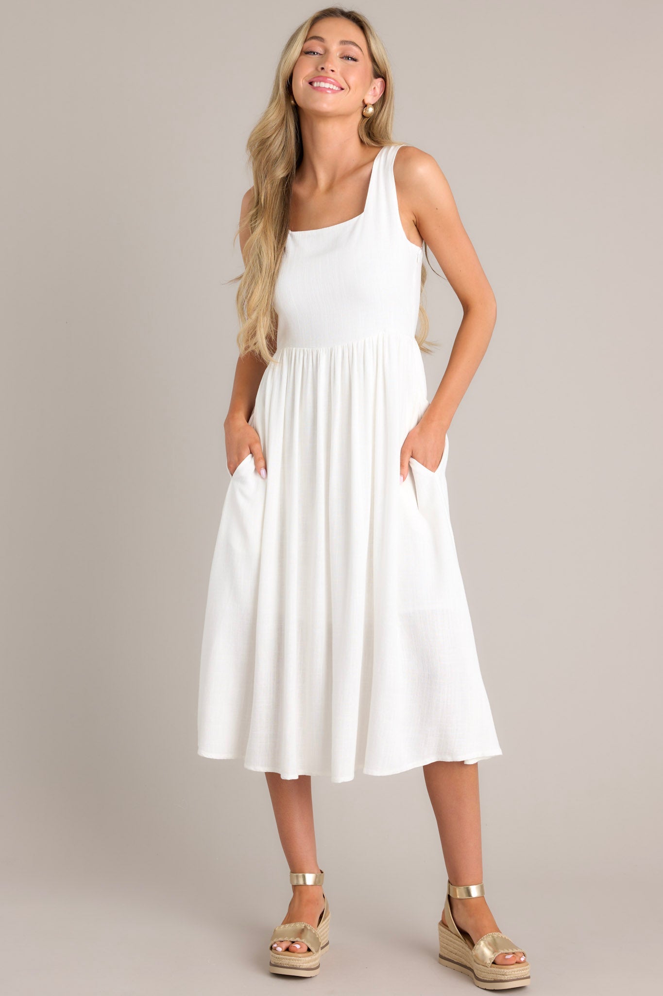 This dress features a square neckline, thick straps, a smocked back insert, a discrete side zipper, gathering at the waist, and functional hip pockets.