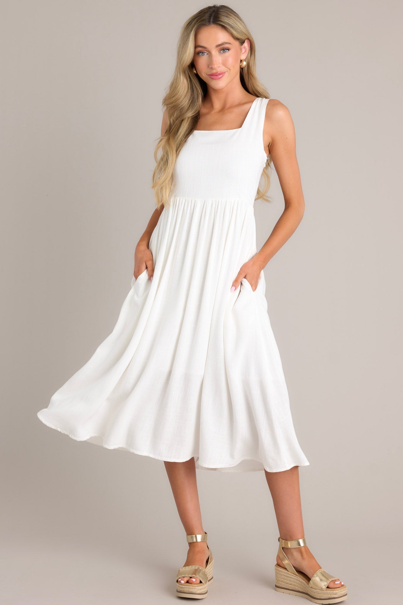 Full body view of this white dress with a square neckline, thick straps, smocked back insert, side zipper, waist gathering, and hip pockets.