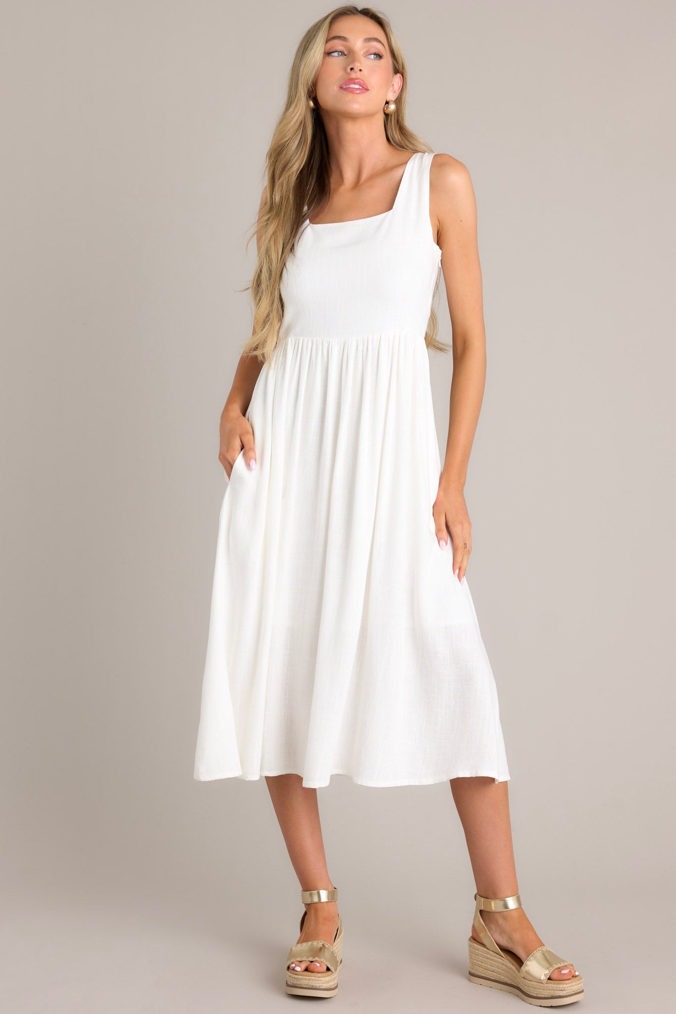 Front view of this white dress with a square neckline, thick straps, smocked back insert, side zipper, waist gathering, and hip pockets.