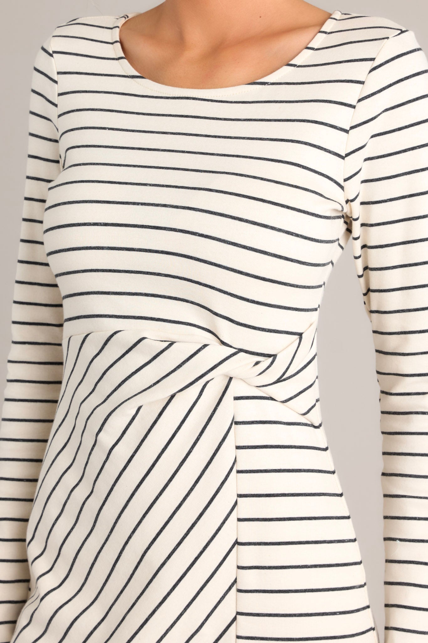 Close up view of this dress featuring a crew neckline, a fitted waistline with a twist detail on the side, a side slit up the leg, long sleeves, and a striped pattern throughout.