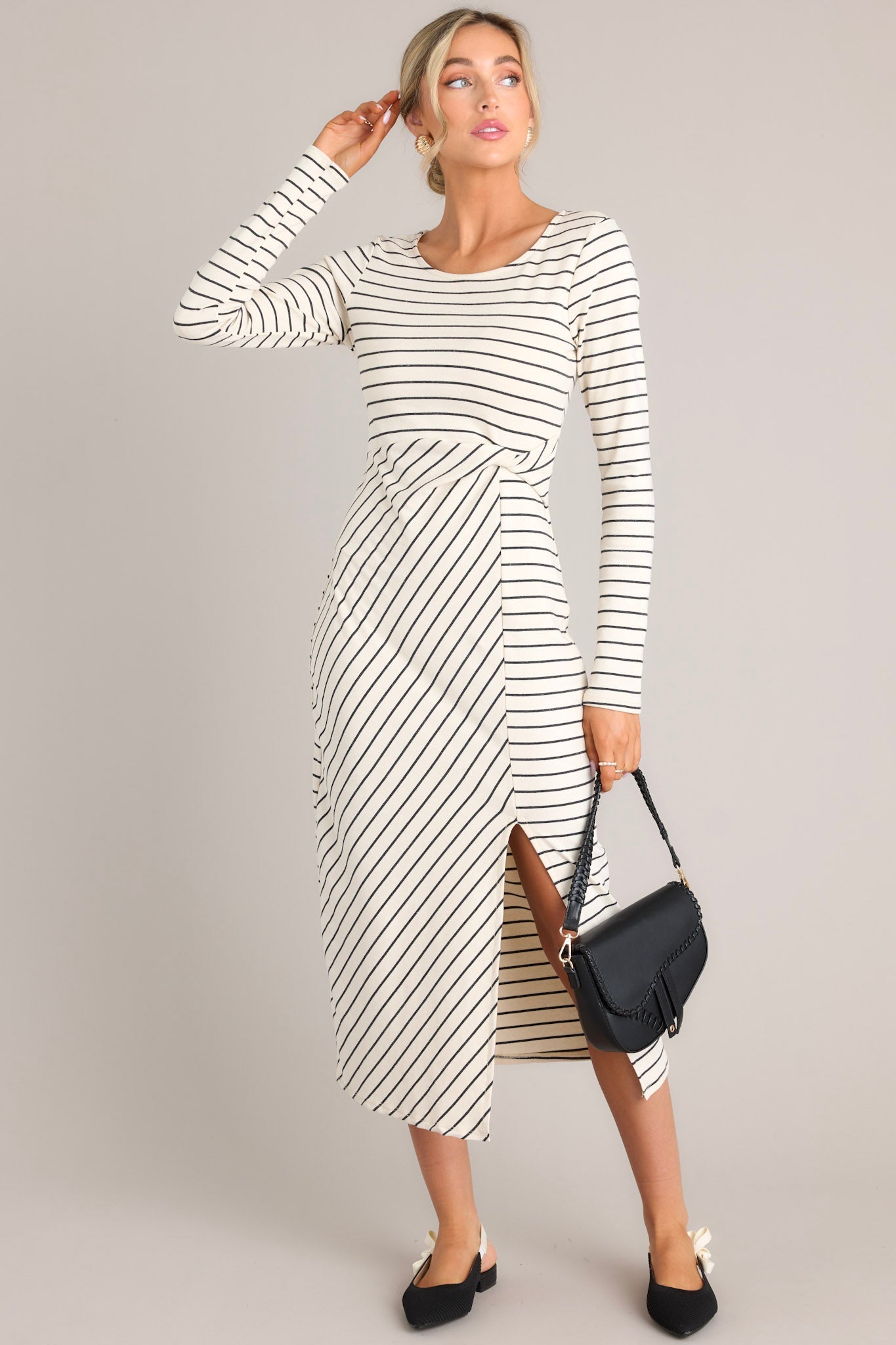 Full body view of this dress that features a crew neckline, a fitted waistline with a twist detail on the side, a side slit up the leg, long sleeves, and a striped pattern throughout.