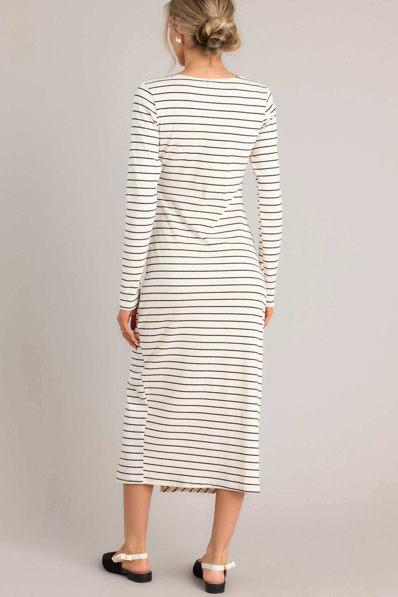 Back view of this dress that features a crew neckline, a fitted waistline with a twist detail on the side, a side slit up the leg, long sleeves, and a striped pattern throughout.