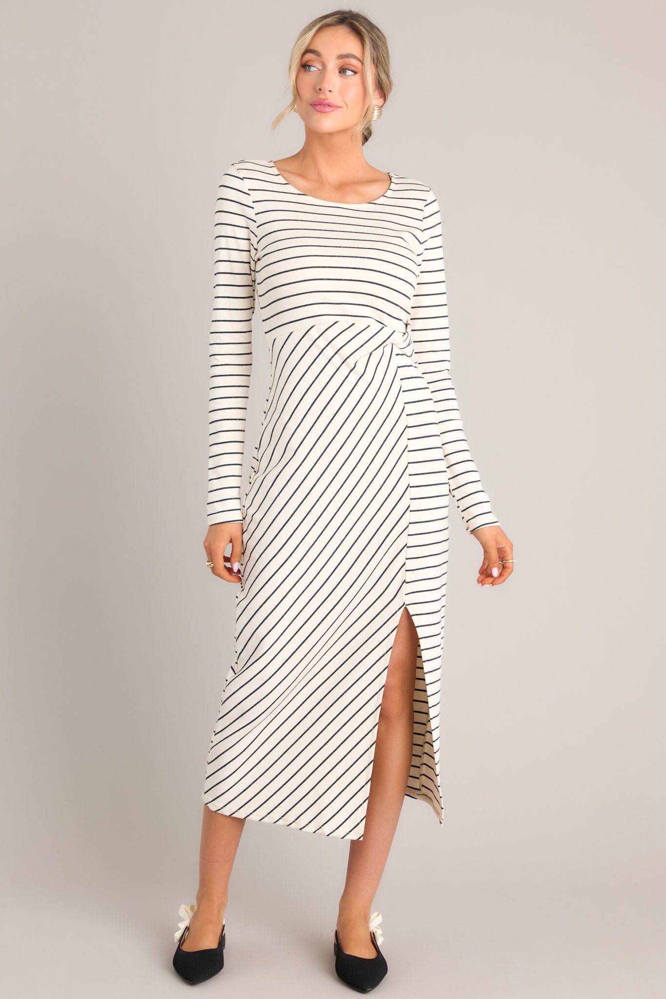 Front view of this dress features a crew neckline, a fitted waistline with a twist detail on the side, a side slit up the leg, long sleeves, and a striped pattern throughout.