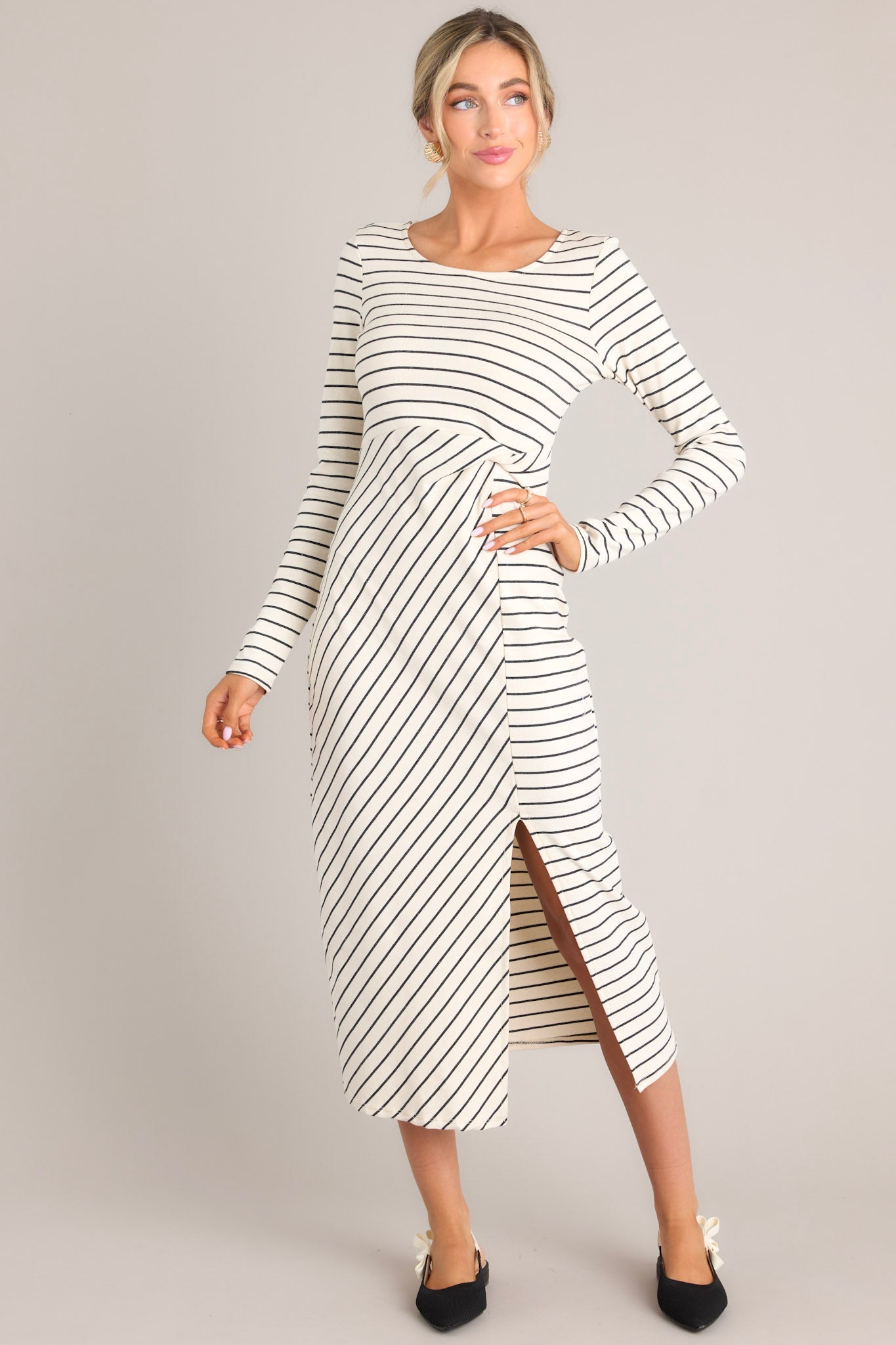 This ivory stripe dress features a crew neckline, a fitted waistline with a twist detail on the side, a side slit up the leg, long sleeves, and a striped pattern throughout.
