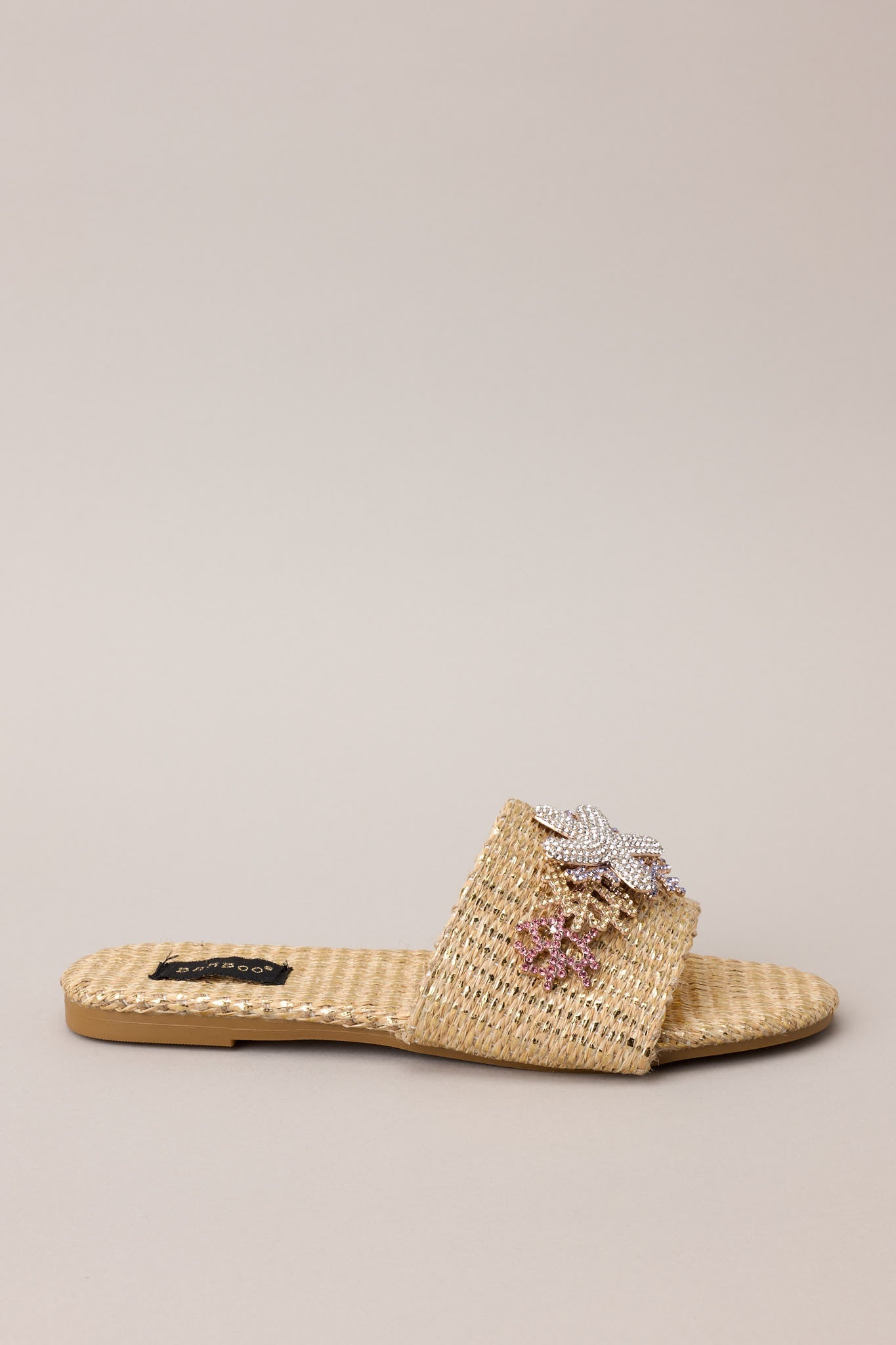 Close up view of these sandals that feature a rounded toe, a slip-on design, a wicker-like material, and tropical multicolored rhinestone detailing.