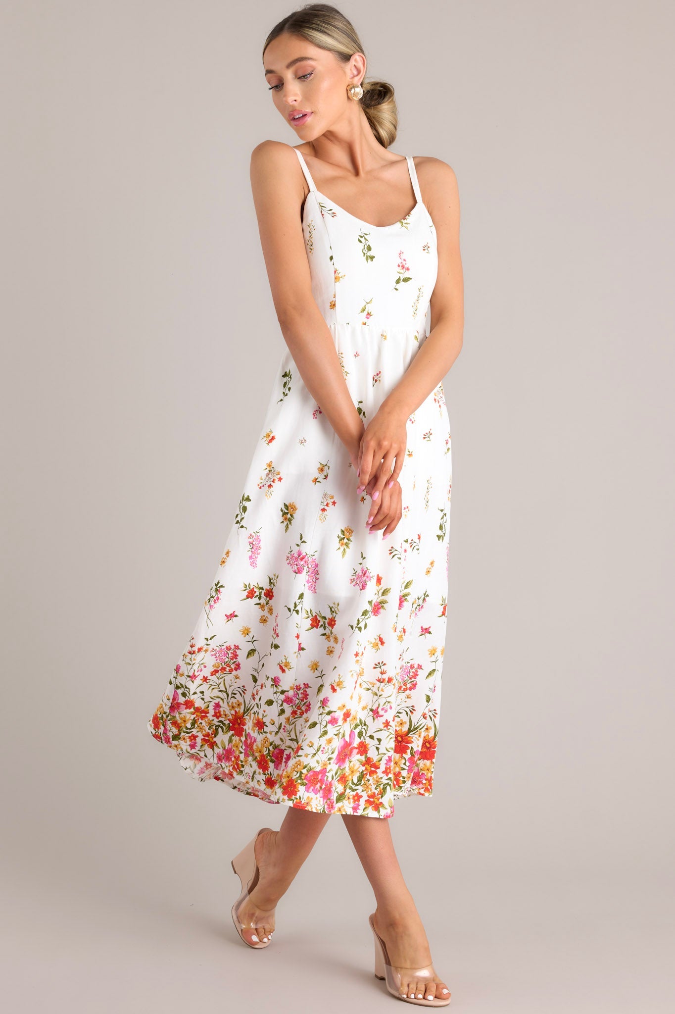 Ivory midi dress adorned with delicate floral prints and a fitted bodice, showcasing its flowy skirt and thin straps, paired with clear wedge heels.