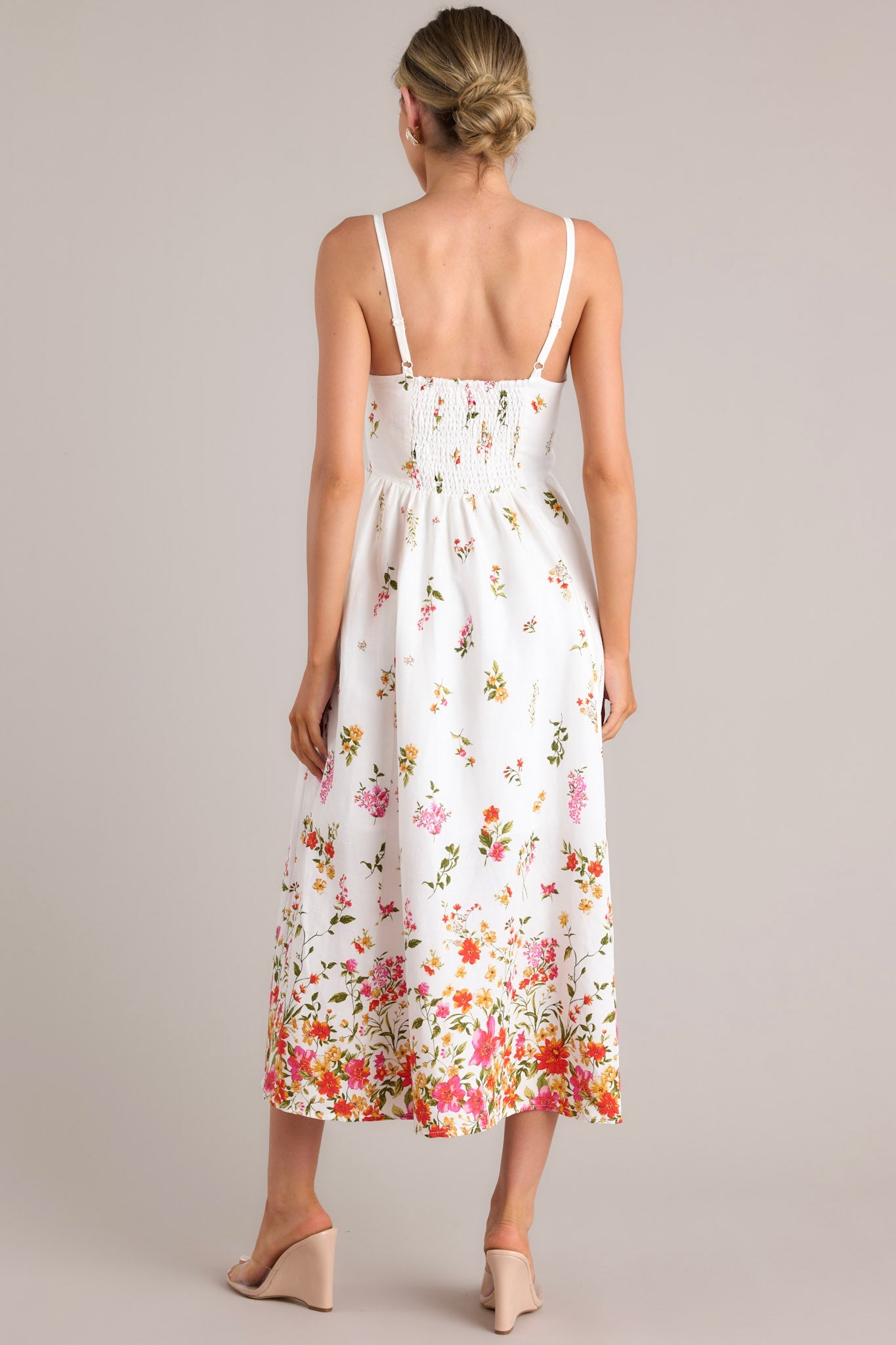 Back view of this ivory floral midi dress featuring a smocked back and adjustable thin straps, showcasing the vibrant floral border at the hem.