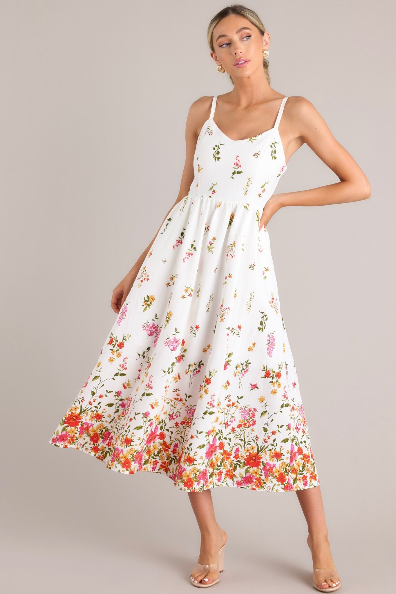 Ivory floral midi dress with a fitted bodice and a flared skirt, featuring a colorful botanical border, paired with clear block heels.