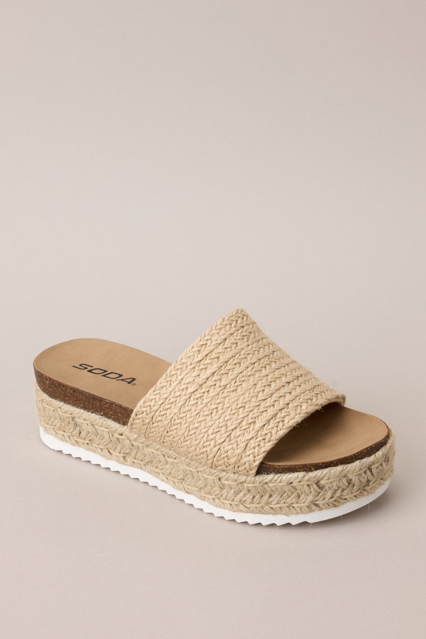 Angled front view of these natural sandals with rounded toe, slip-on design, strap over foot, espadrille detailing, textured sole.