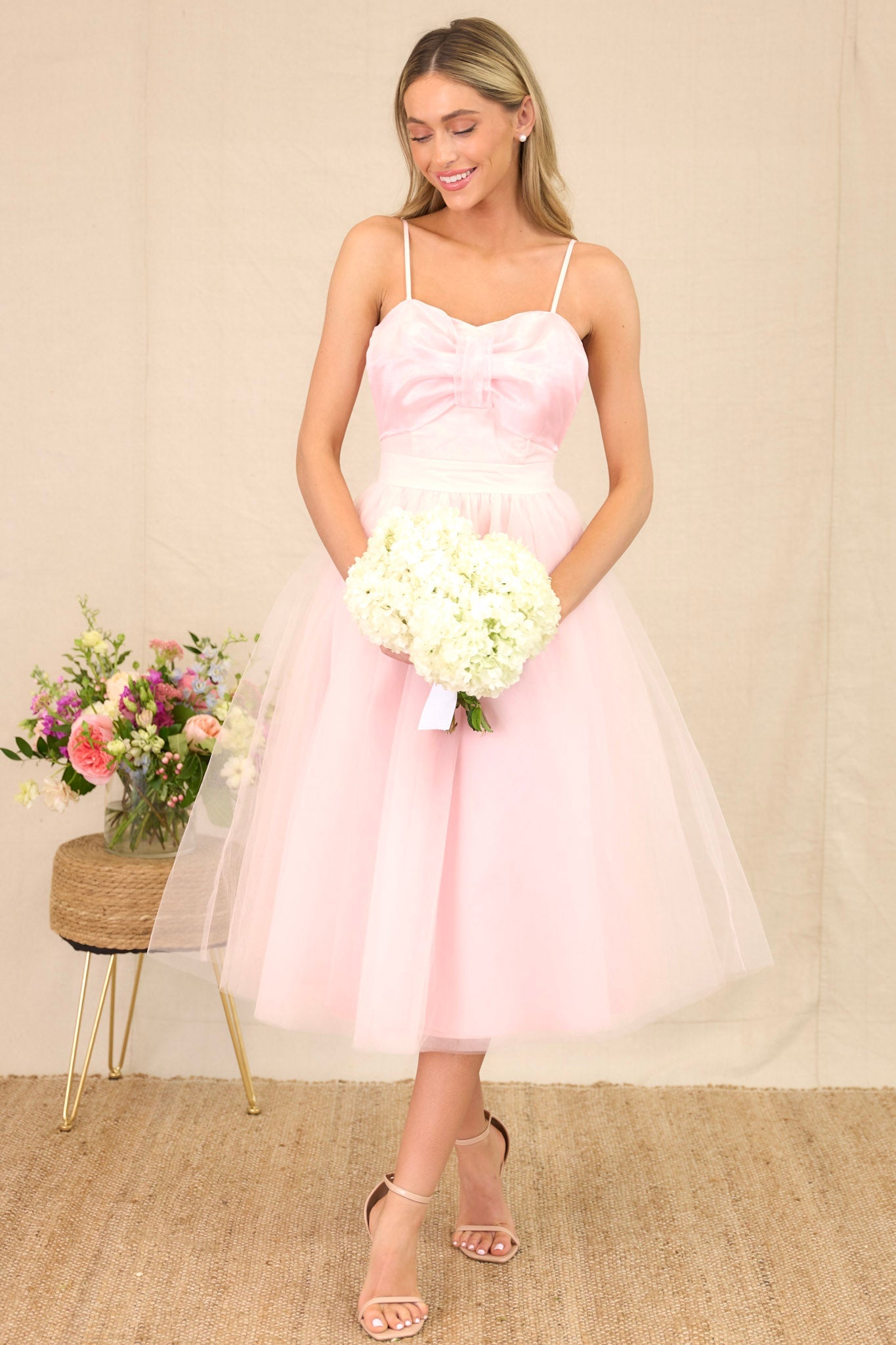 Front angled view of a tulle dress featuring a sweetheart neckline with a built-in bow detail, skinny adjustable shoulder straps, a corset-style bust, a voluminous tulle skirt, and a back zipper closure