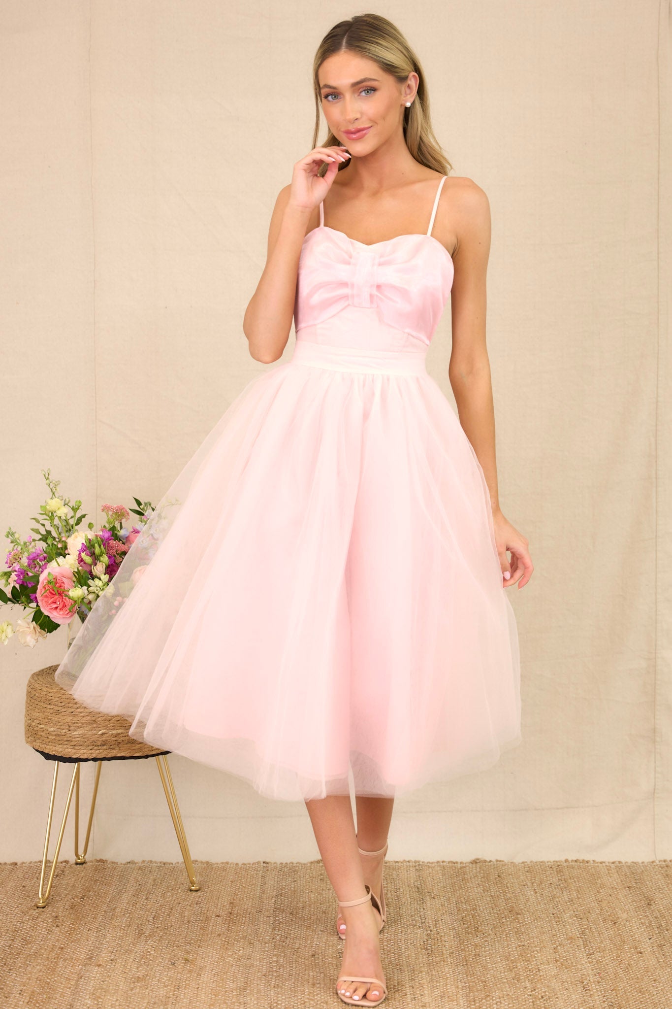 Front view of a tulle dress featuring a sweetheart neckline with a built-in bow detail, skinny adjustable shoulder straps, a corset-style bust, a voluminous tulle skirt, and a back zipper closure.