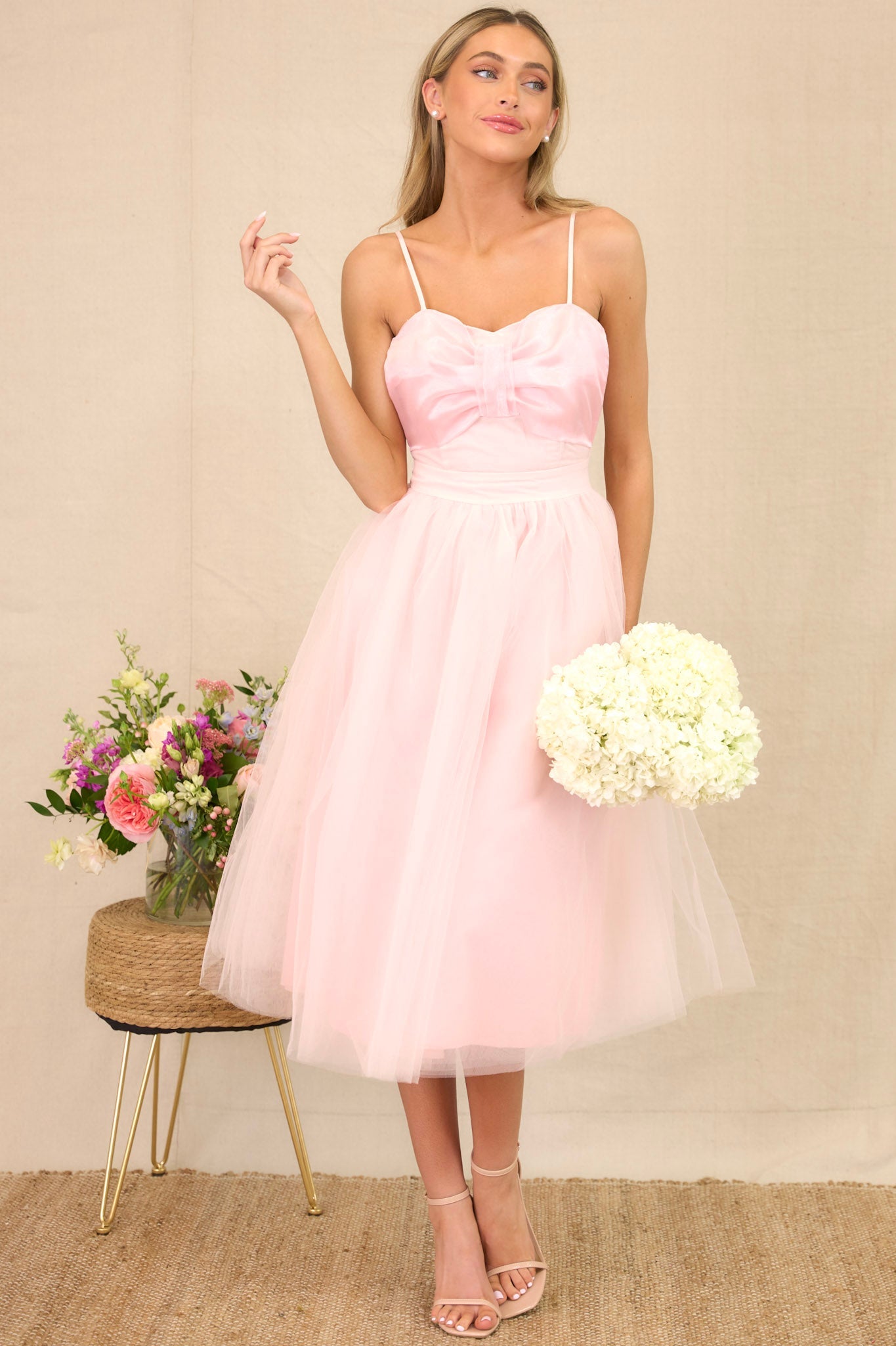 Full length view of a tulle dress featuring a sweetheart neckline with a built-in bow detail, skinny adjustable shoulder straps, a corset-style bust, a voluminous tulle skirt, and a back zipper closure