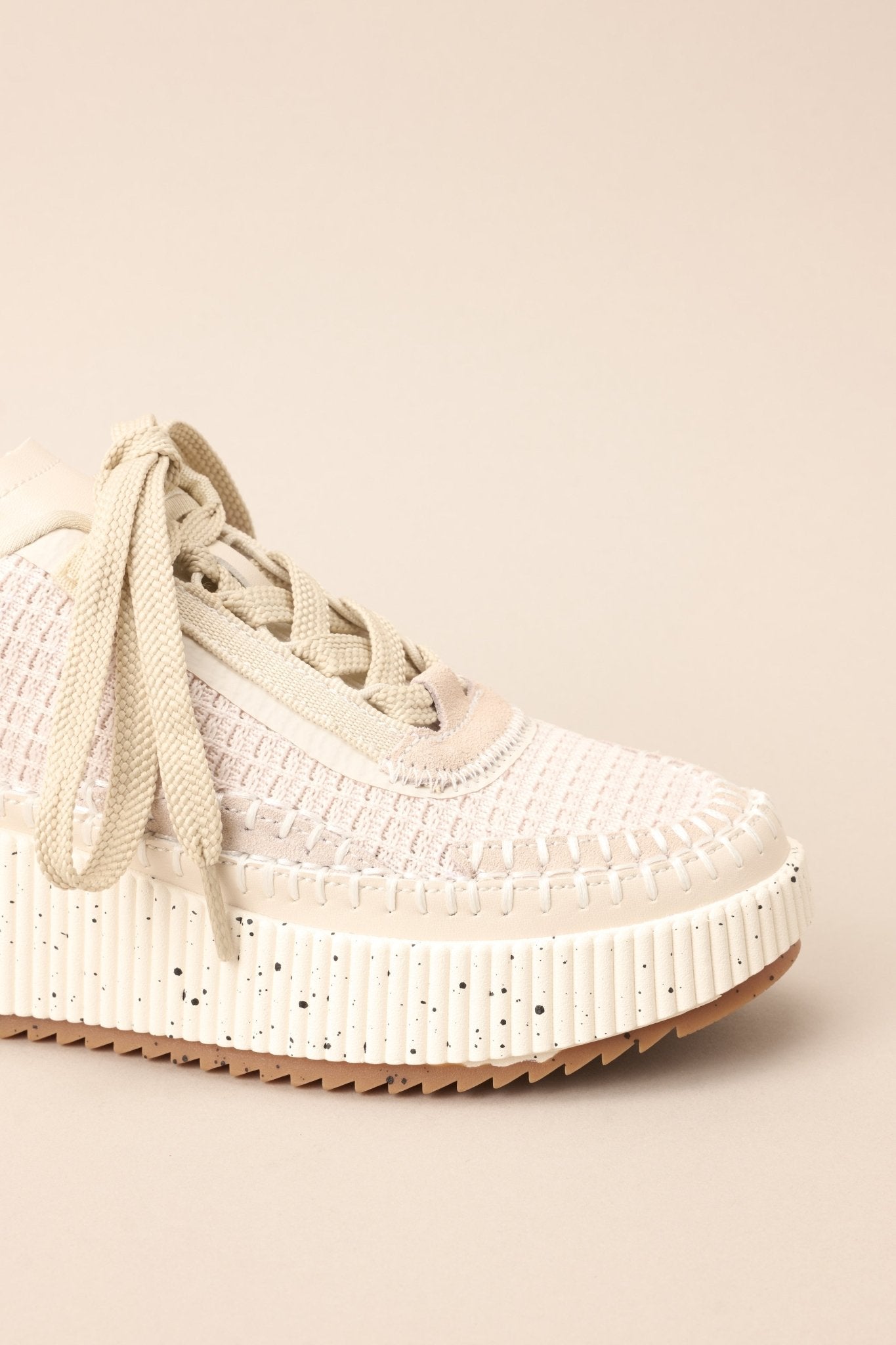 Close view of these beige sneakers with rounded toe, functional laces, knitted detailing, comfortable fit, thick speckled sole.