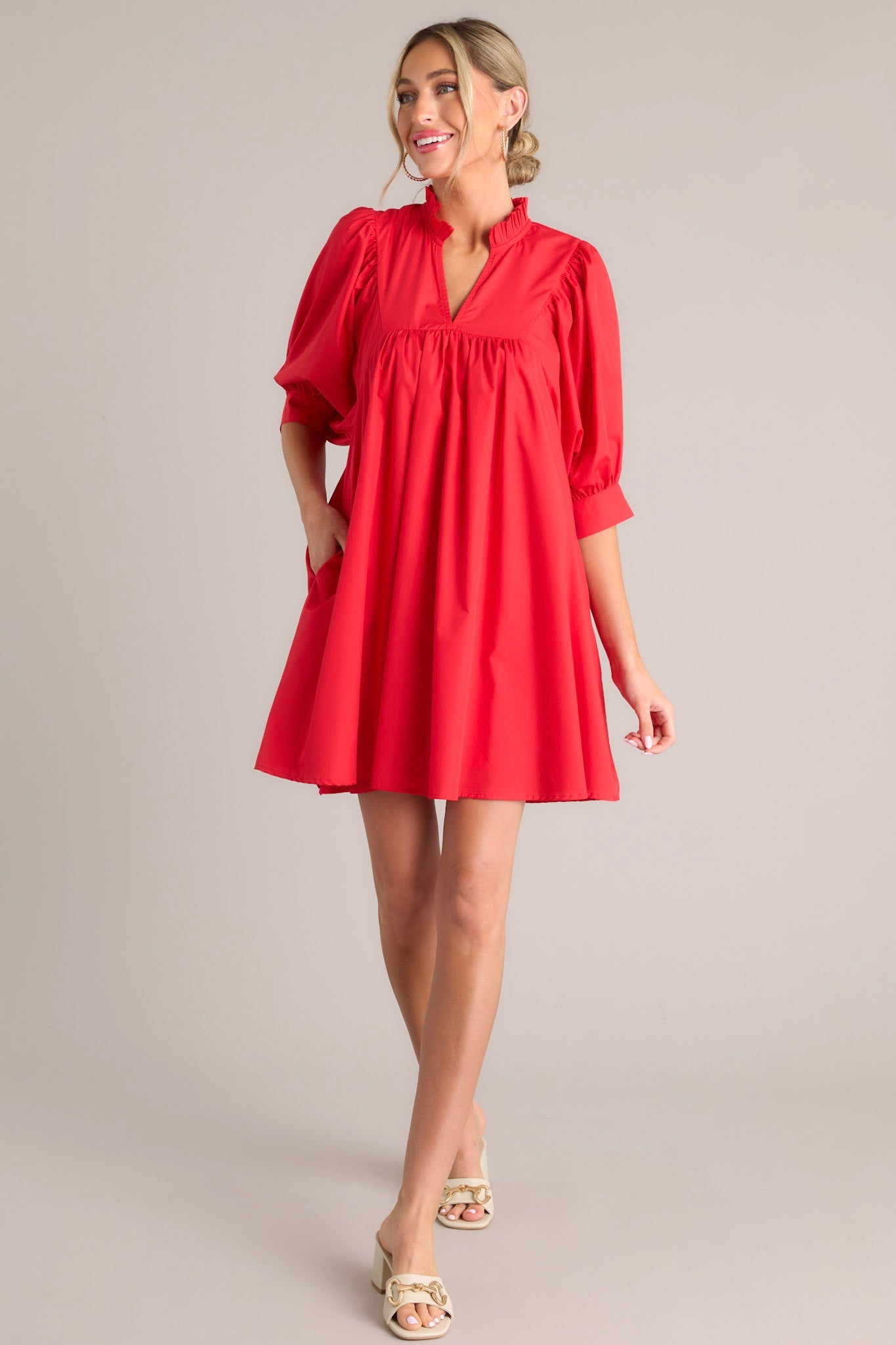 Full body view of this red mini dress that features a v-neckline, a ruffled faux collar, pleated detailing around the bust, functional hip pockets, and cuffed puff sleeves.