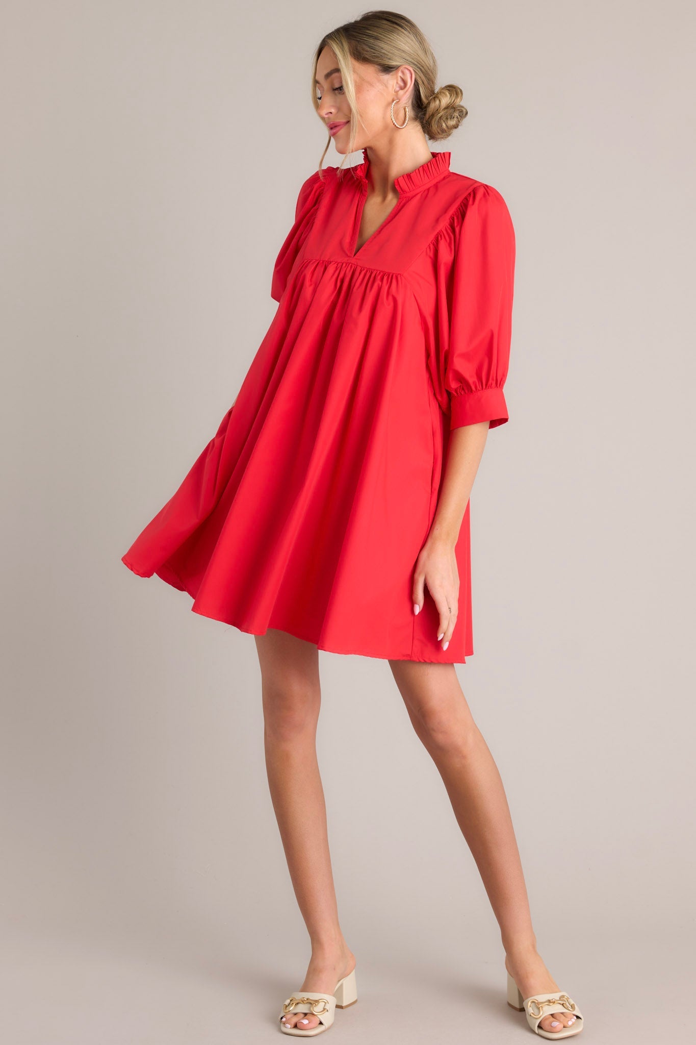 Side view of this red mini dress that features a v-neckline, a ruffled faux collar, pleated detailing around the bust, functional hip pockets, and cuffed puff sleeves.