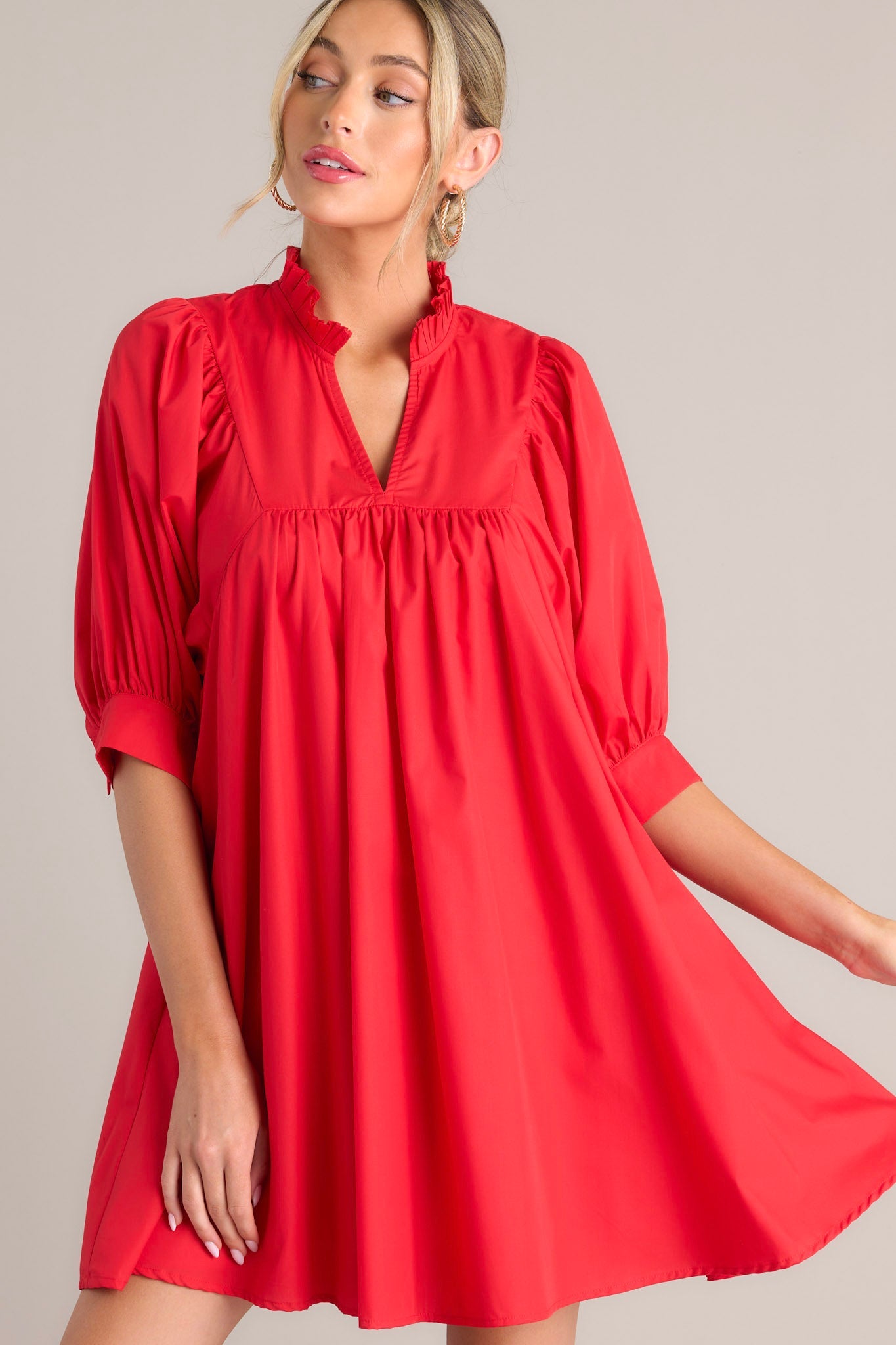 Close up front view of this red mini dress that features a v-neckline, a ruffled faux collar, pleated detailing around the bust, functional hip pockets, and cuffed puff sleeves.