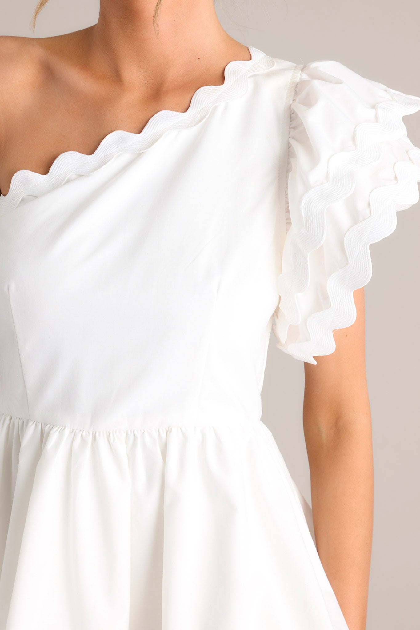 Close-up of the white romper showing the rick rack scalloped hems, one shoulder neckline, and flutter sleeve