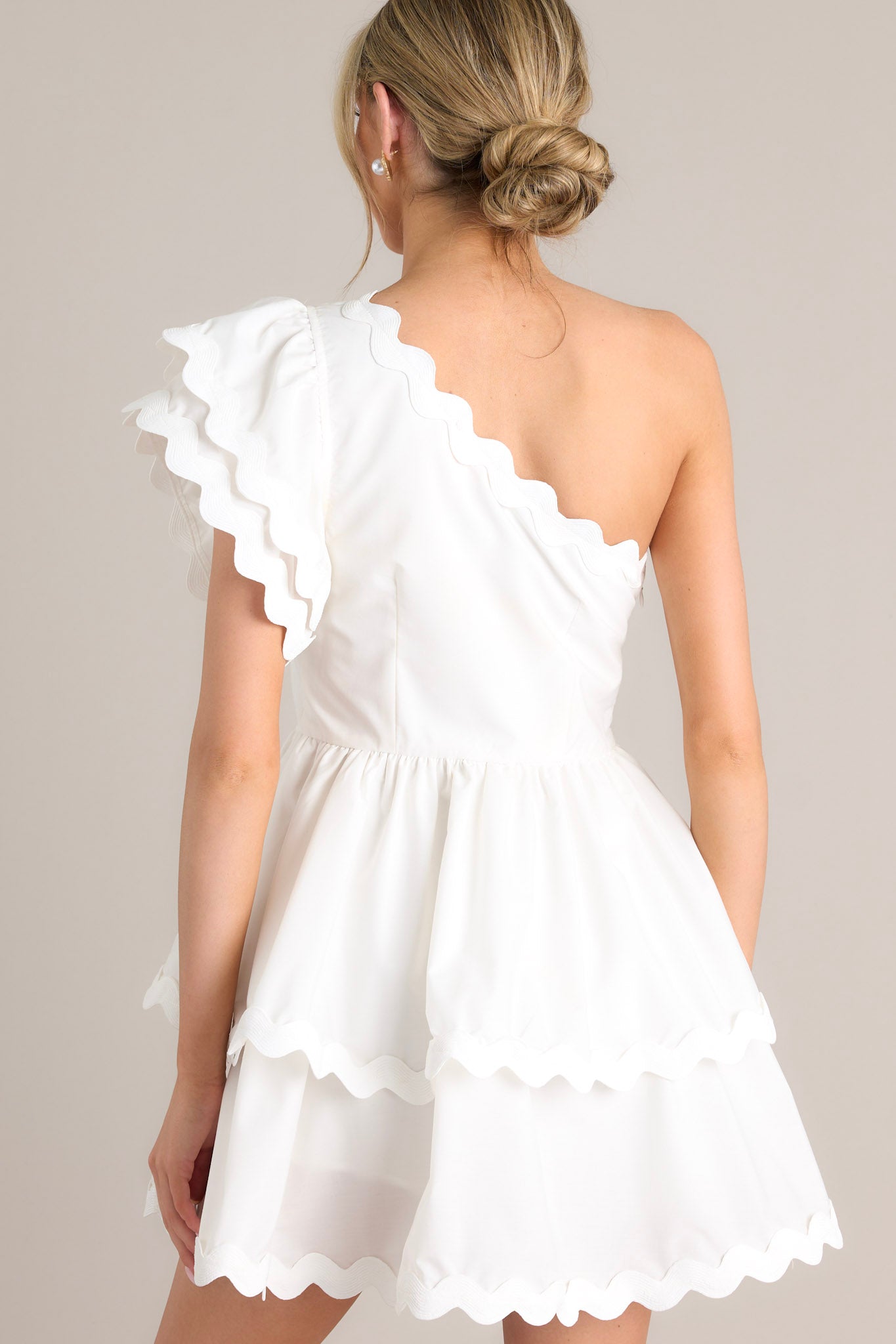 Back view of a white romper highlighting the side zipper closure, tiered skirt with built-in shorts, and rick rack scalloped hems.