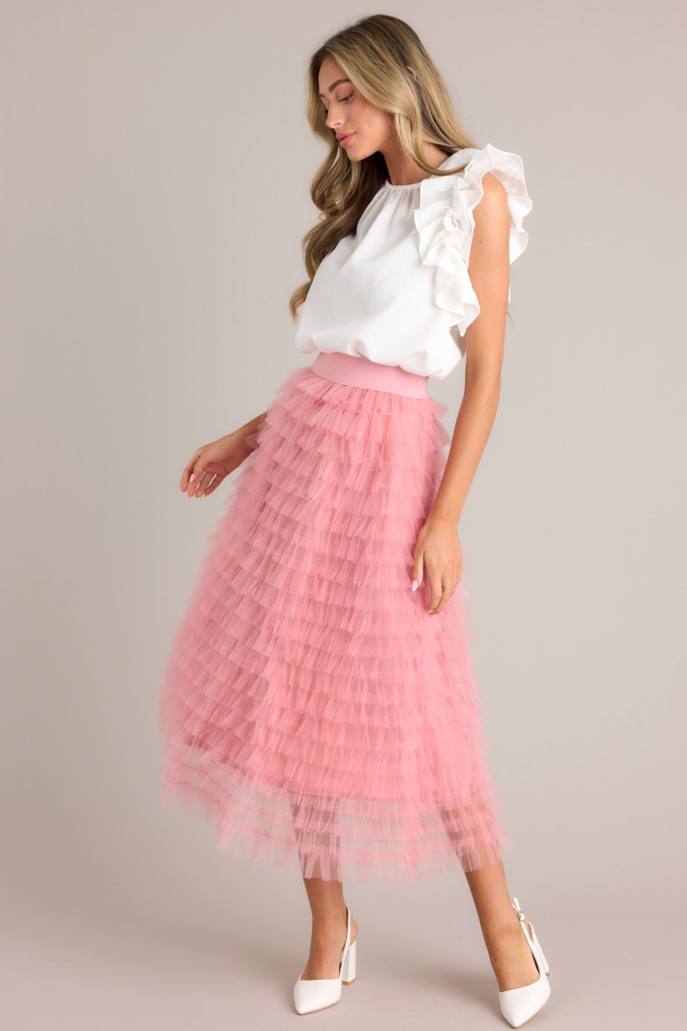 Angled front view of this pink skirt that features a high-waist design with an elastic waistband for a comfortable fit, adorned with charming ruffle tulle detailing throughout.