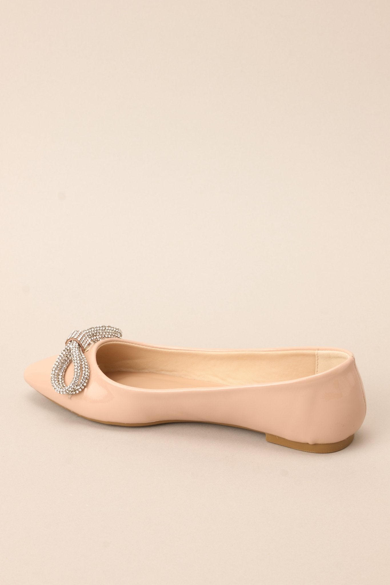 Angled view of these chic flats with a pointed toe, adorned with a dazzling rhinestone-embellished bow, and finished with a shiny sheen.