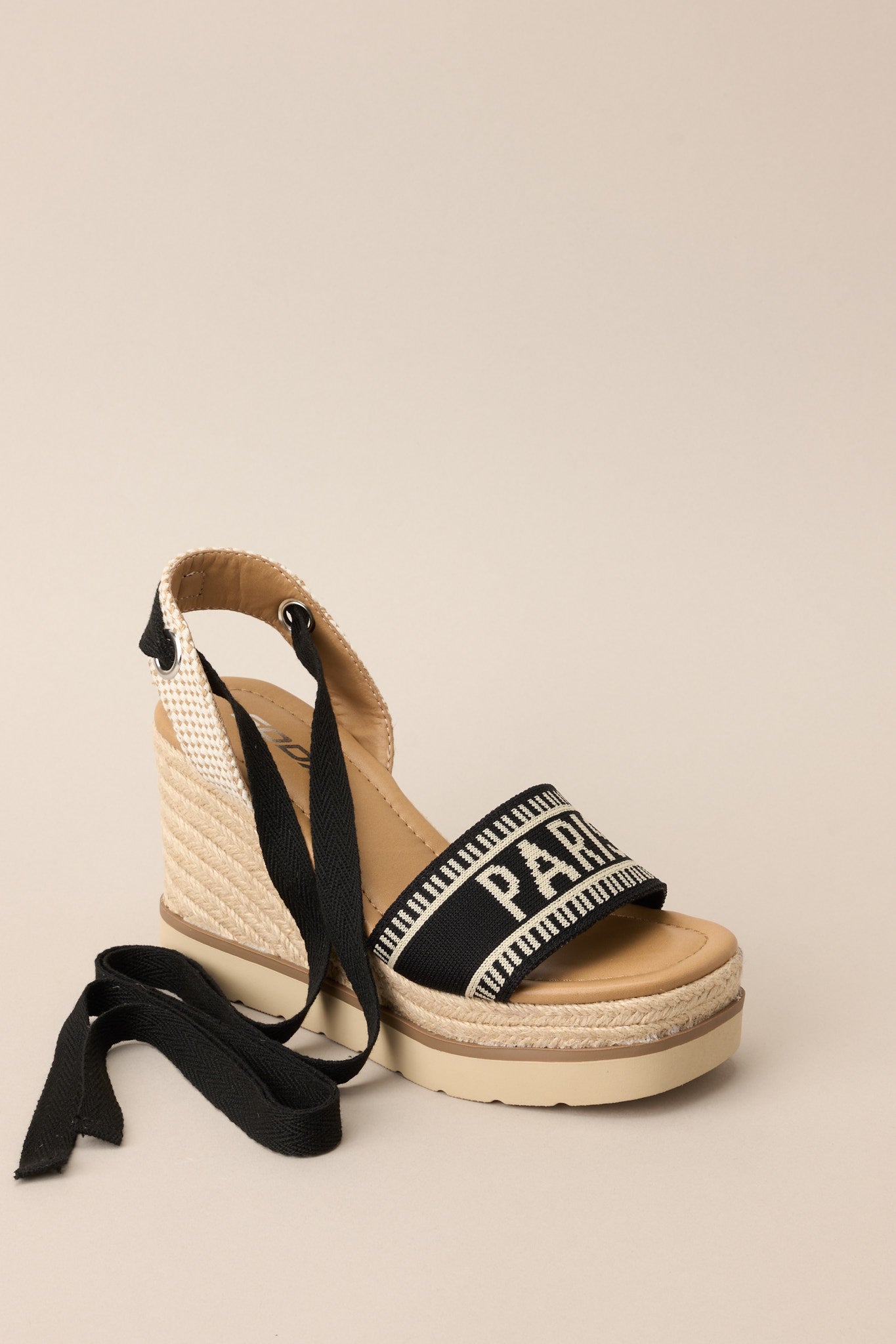 Angled front view of these black platform wedge sandals that feature a rounded toe, a strap over the top of the foot and around the heel, adjustable self-tie straps around the ankle, and a wedged heel.